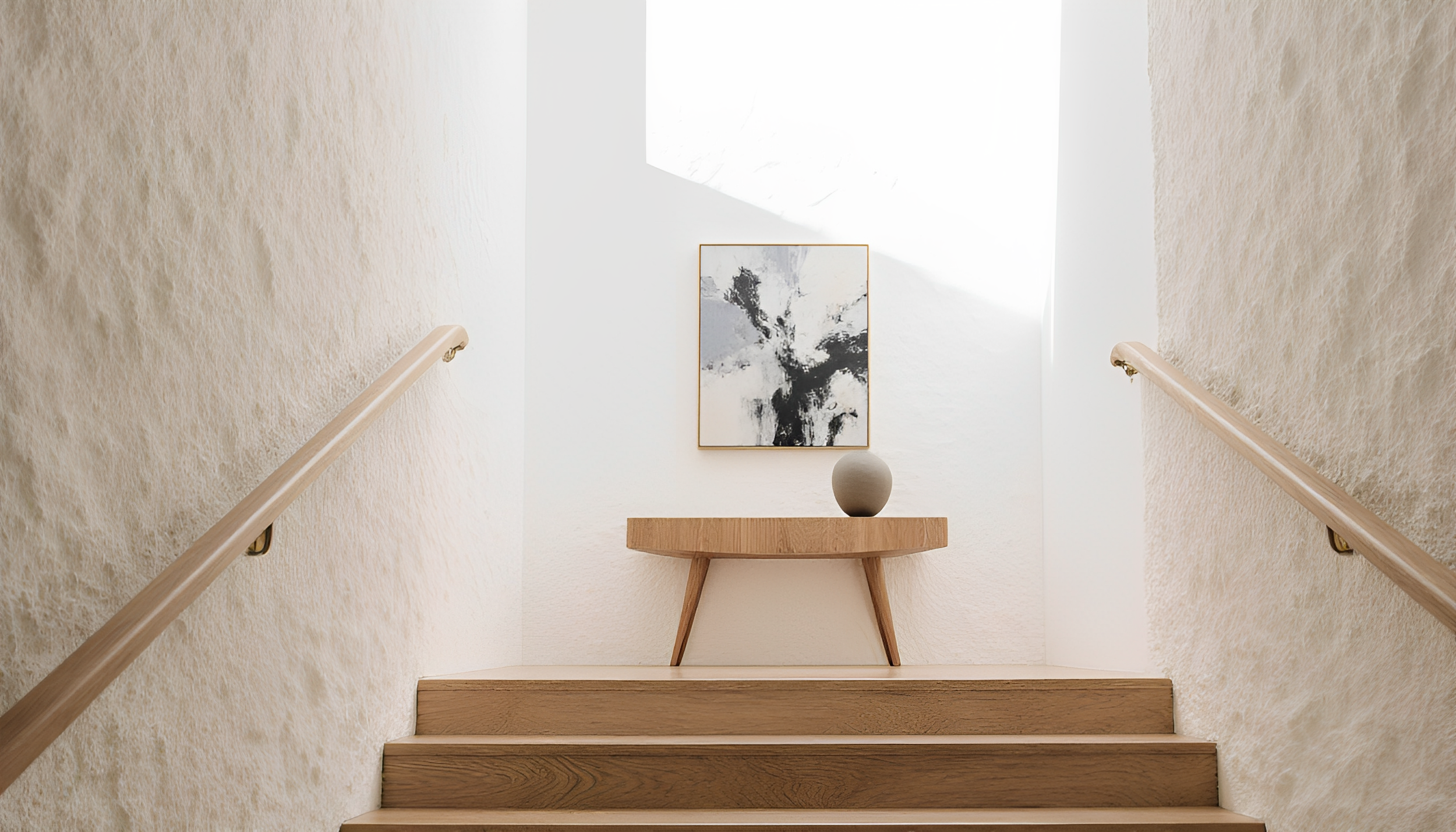 Interior view of a staircase with beige walls and wooden steps, a round wooden table at the top with a gray vase, and a black and white abstract painting on the wall.