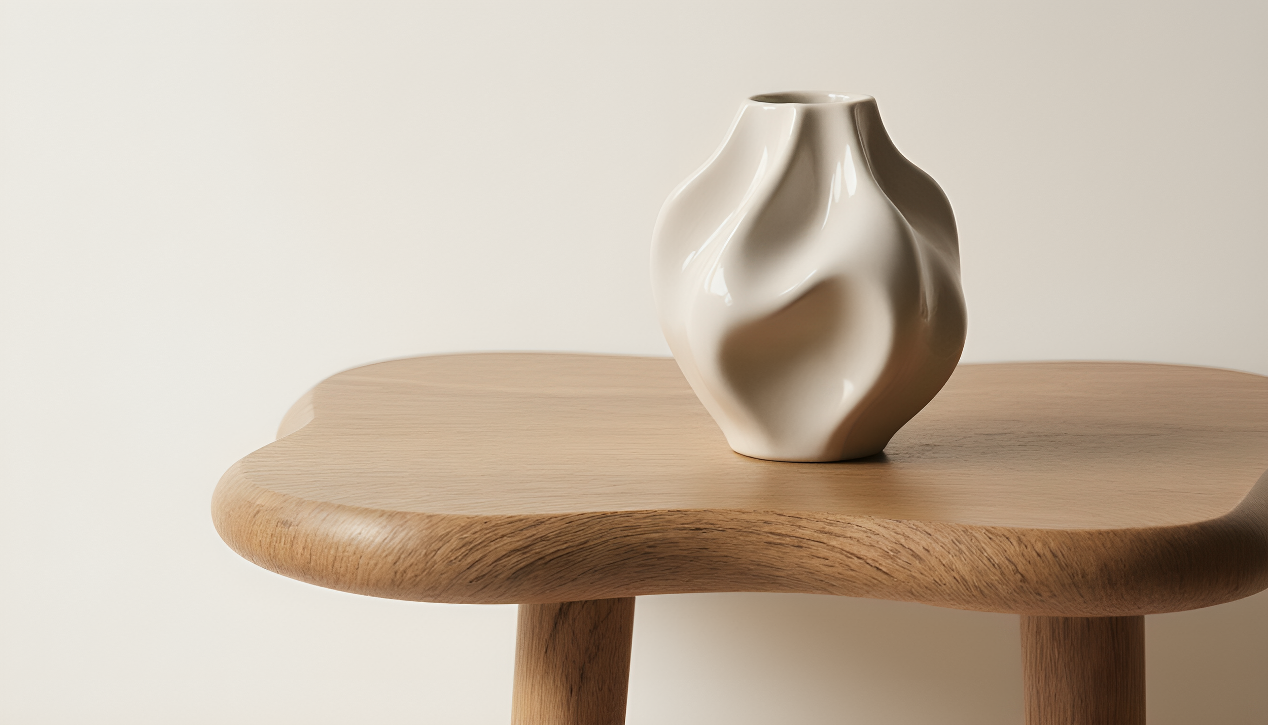 A white ceramic vase with a wavy, abstract shape sits on a round wooden table with a light-colored background.