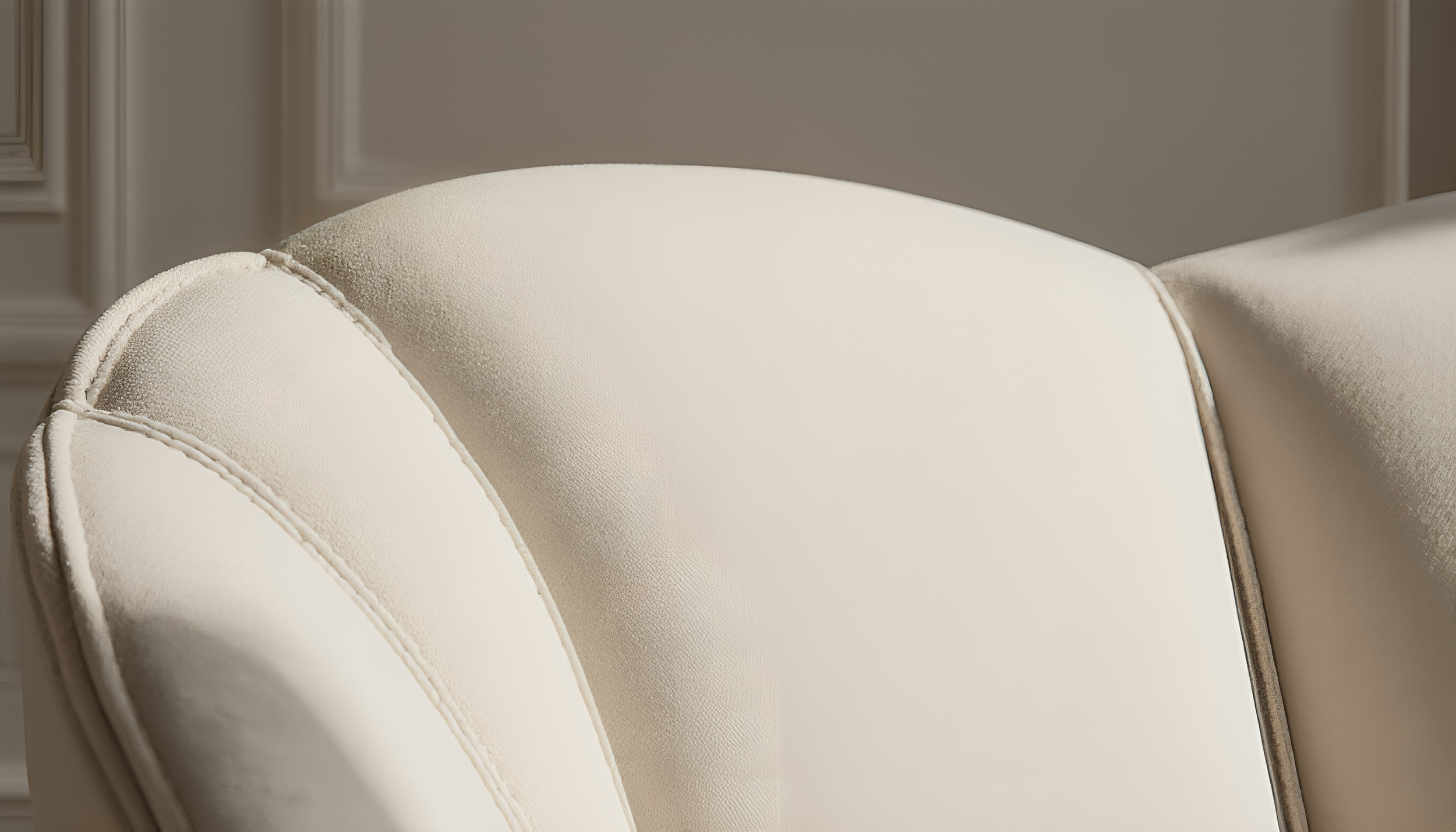 Close-up of a cream-colored armchair with detailed stitching in a softly lit room.