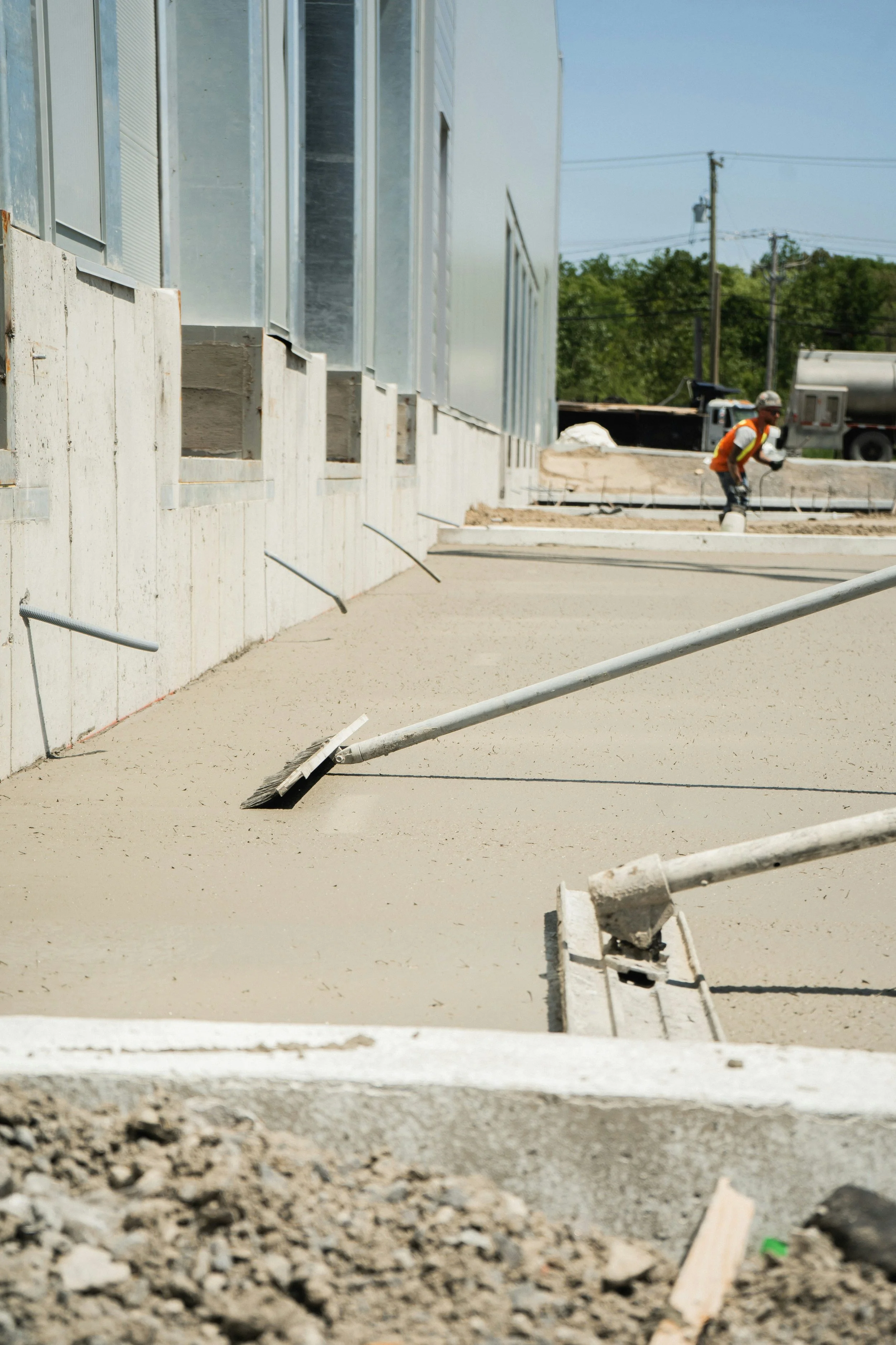 Construction worker wearing a hard hat and safety vest working on a building site with concrete and metal framing.
