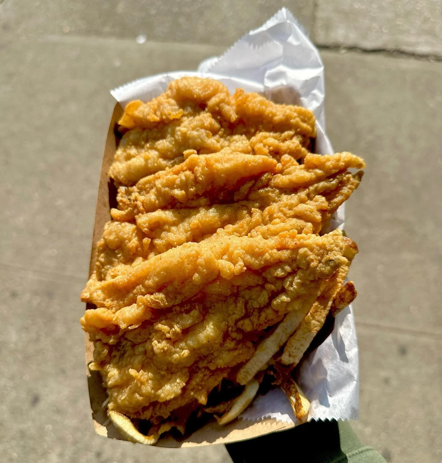 Fried fish fillet served over a bed of French fries in a paper tray.