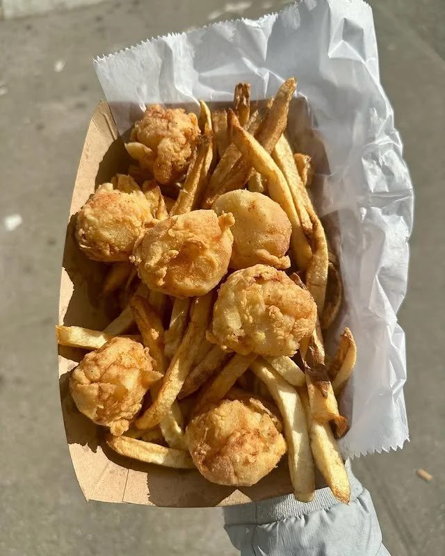 A handheld container of fried chicken pieces and French fries.