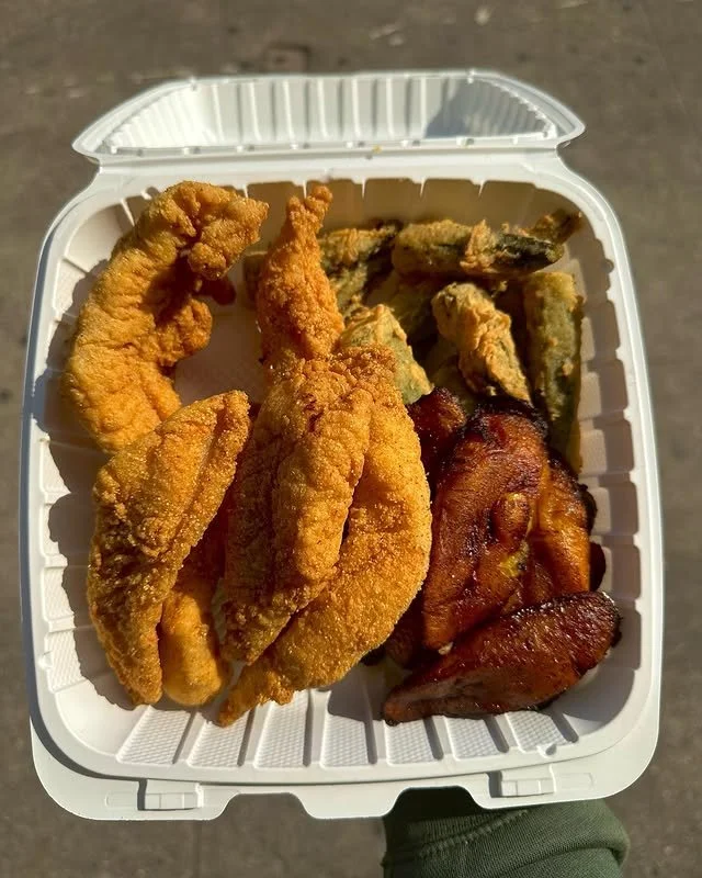 Fried fish fillets, bacon strips, and fried green tomatoes in a white takeout container.