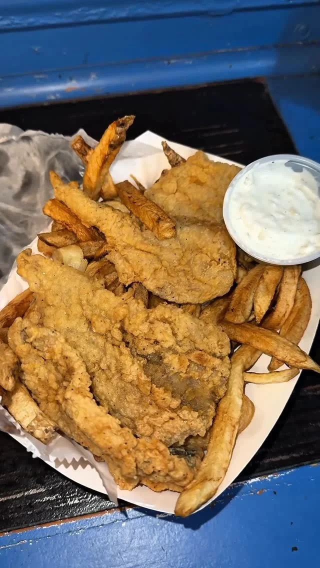 Fried fish fillets with French fries and tartar sauce on a paper-lined tray.