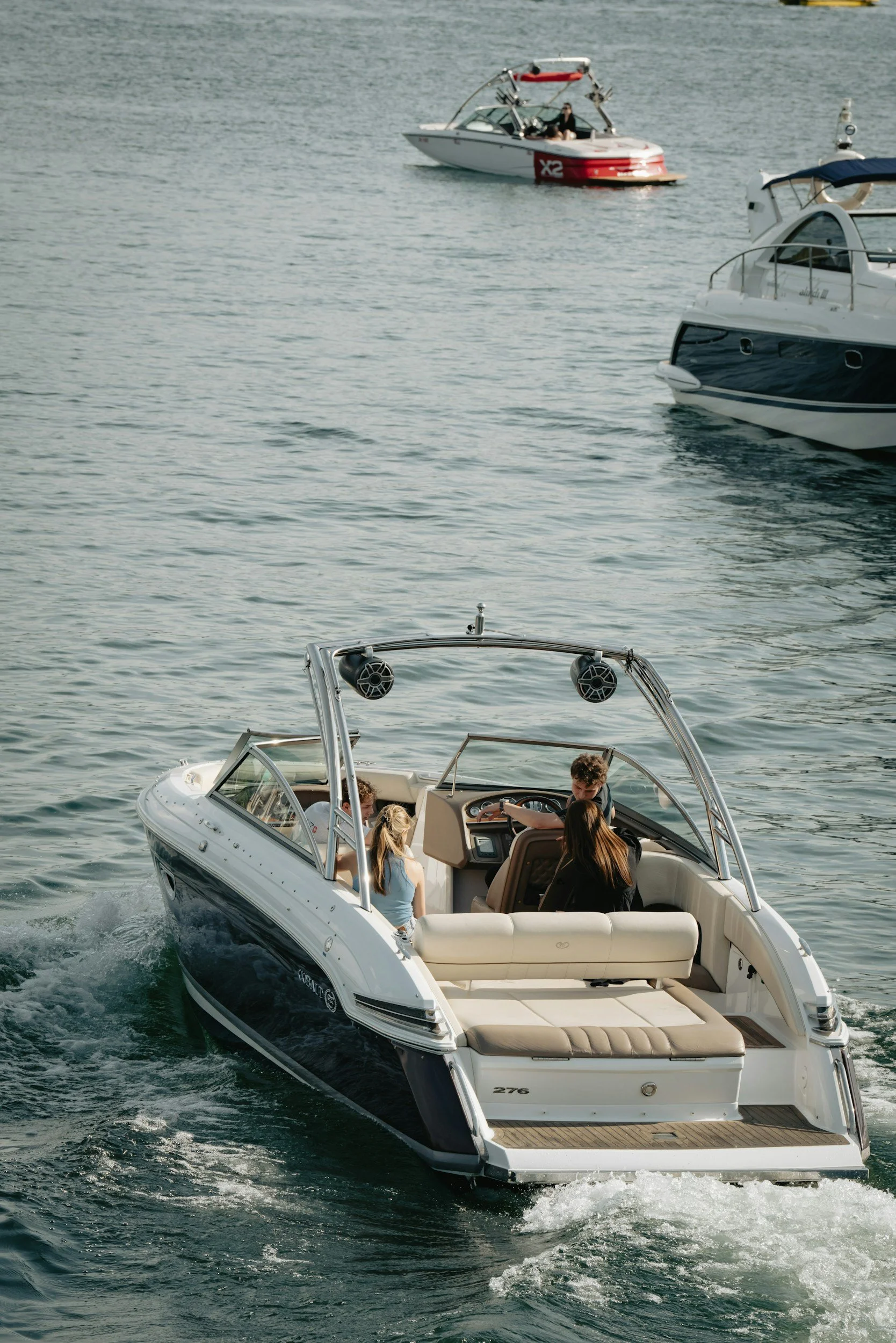 A white motorboat with several people on board, traveling on a body of water with other boats visible in the background.