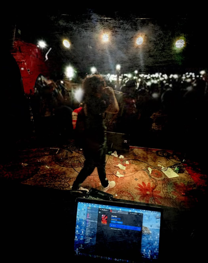 People in a dark room with a DJ setup, colorful lights, and an audience holding up phones with flashlights.