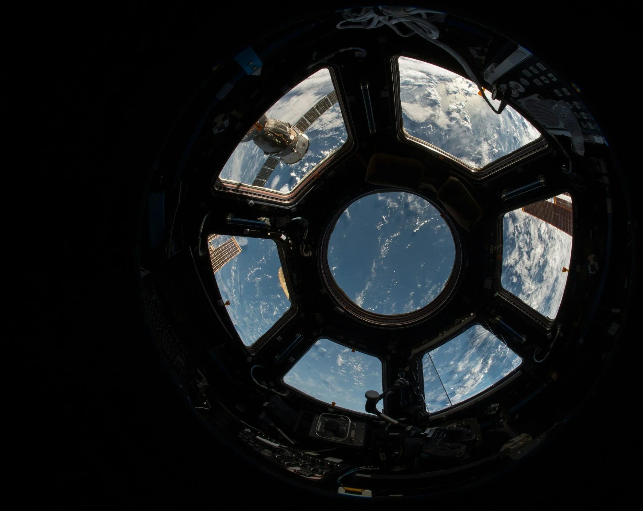 Inside the spacecraft looking out through the observation window at the earth and space, with parts of the spacecraft's interior surrounding the view.