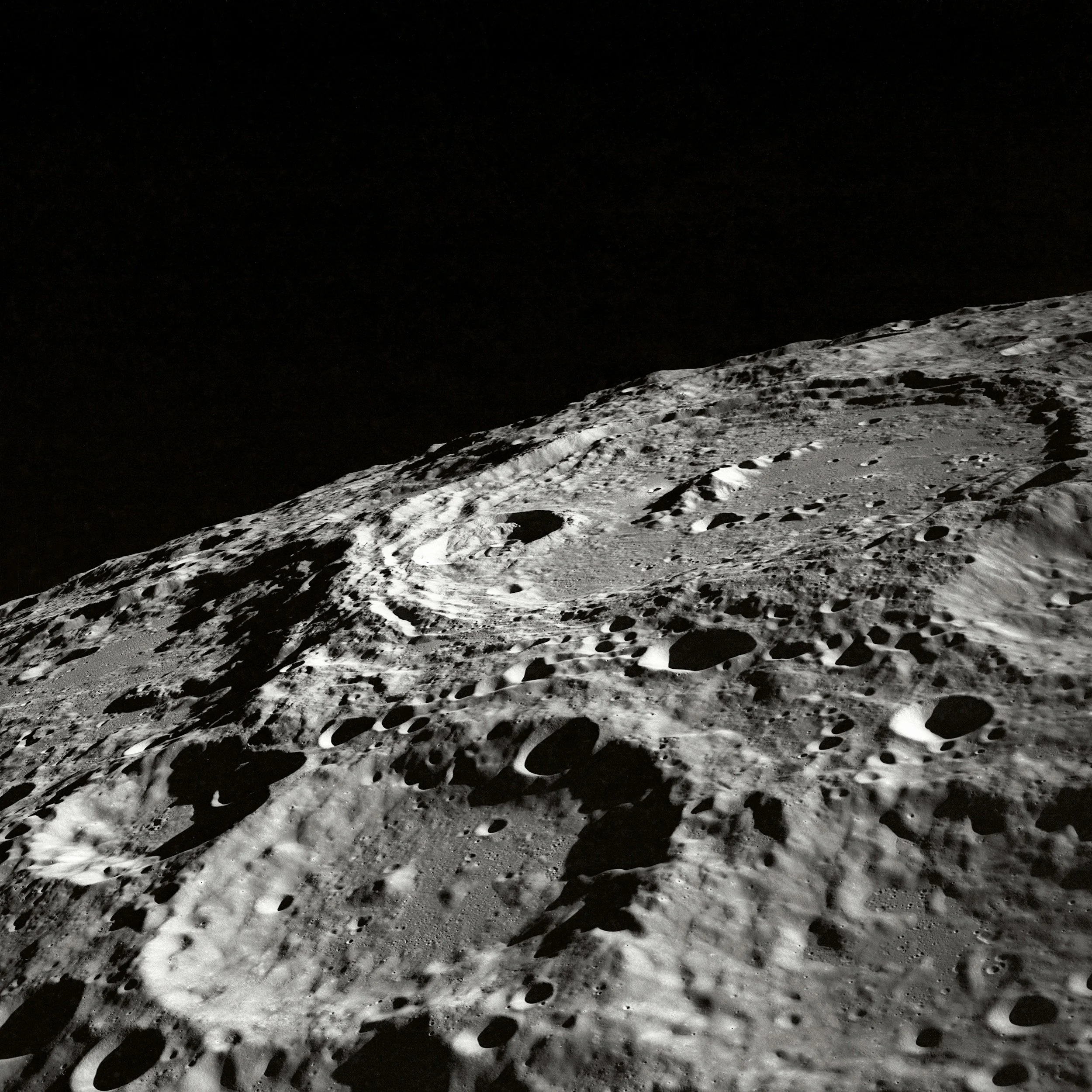 A rocky lunar surface with numerous craters, under a dark sky.