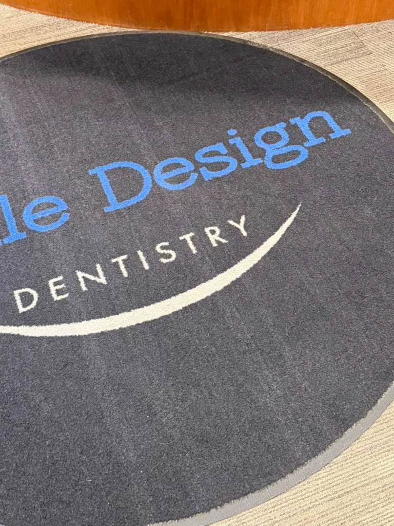 Alfombra circular en el suelo con texto en inglés y español que dice 'de Jim de diseño' y 'odontología'.