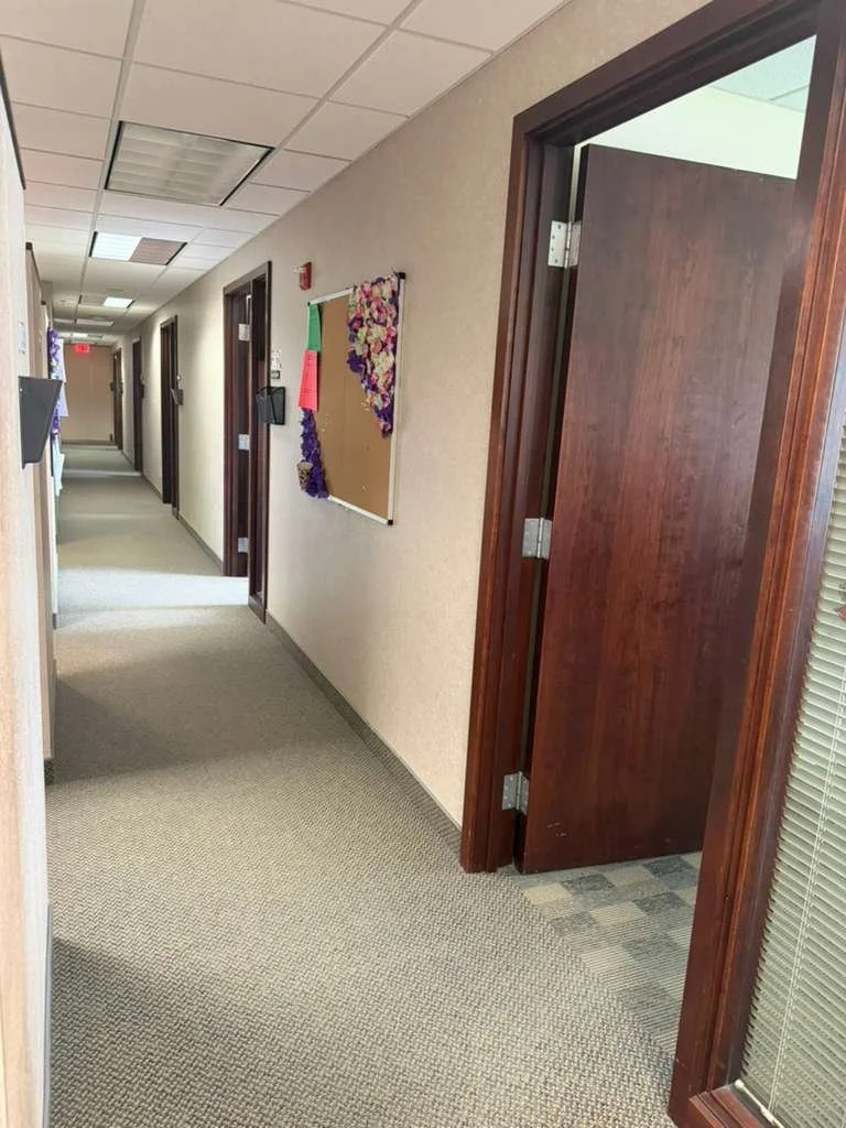 Pasillo en un edificio de oficinas con puertas de madera y una cartelera en la pared decorada con flores de papel.