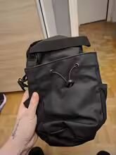 Person holding a black backpack in a room with wooden flooring and white door