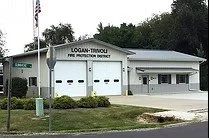 Fire protection station building with signage that reads 'LOGAN TOWNS FIRE PROTECTION DISTRICT' and a garage door in front.