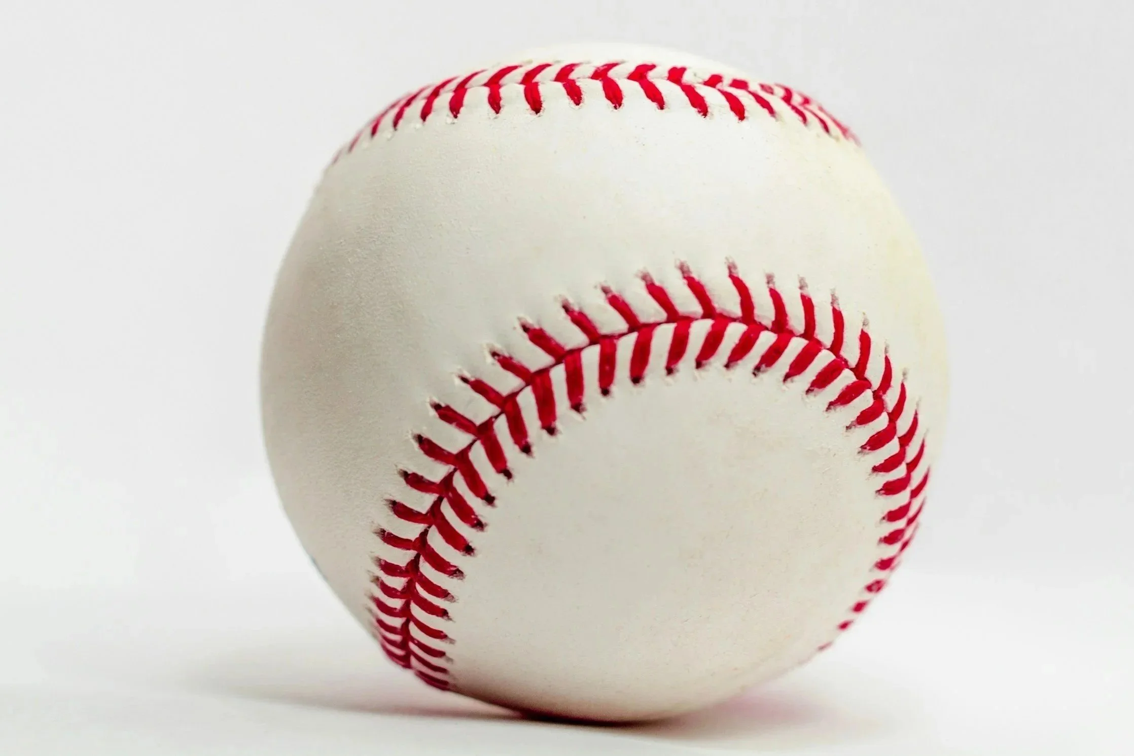 Close-up of a white baseball with red stitching on a white background.