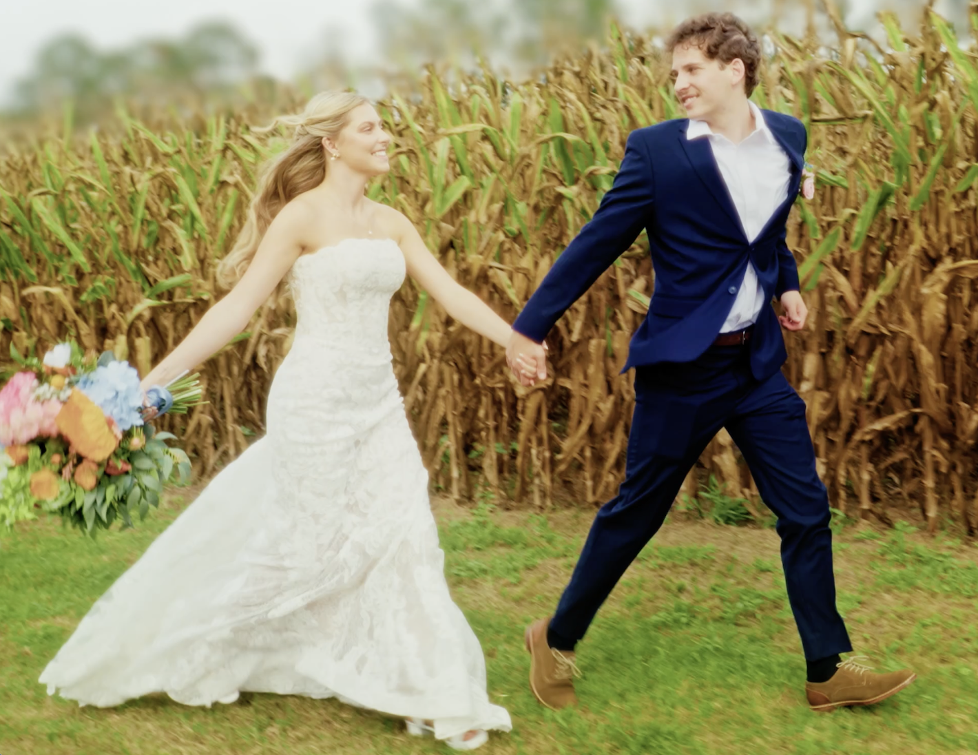 A bride and groom holding hands and running through a field of corn on their wedding day.