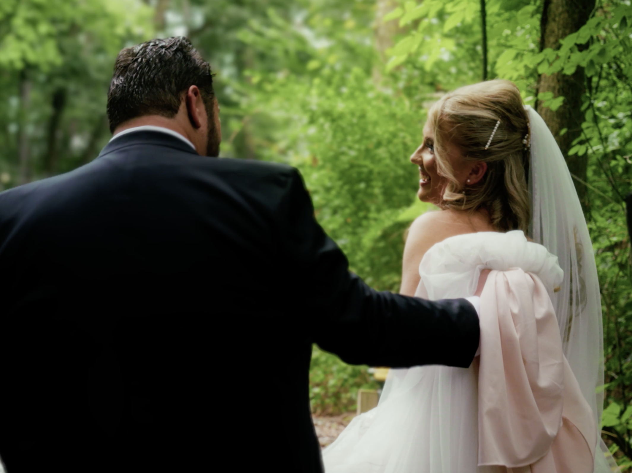 A bride and groom exchanging vows outdoors in a lush green forest with trees and leaves in the background.