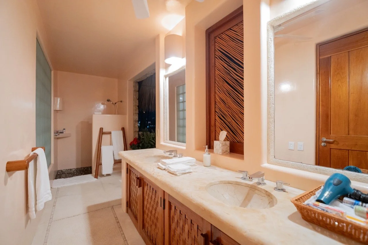 Baño con espejo, lavabo de mármol, toallas, ventanales y accesorios de baño en tonos tierra.