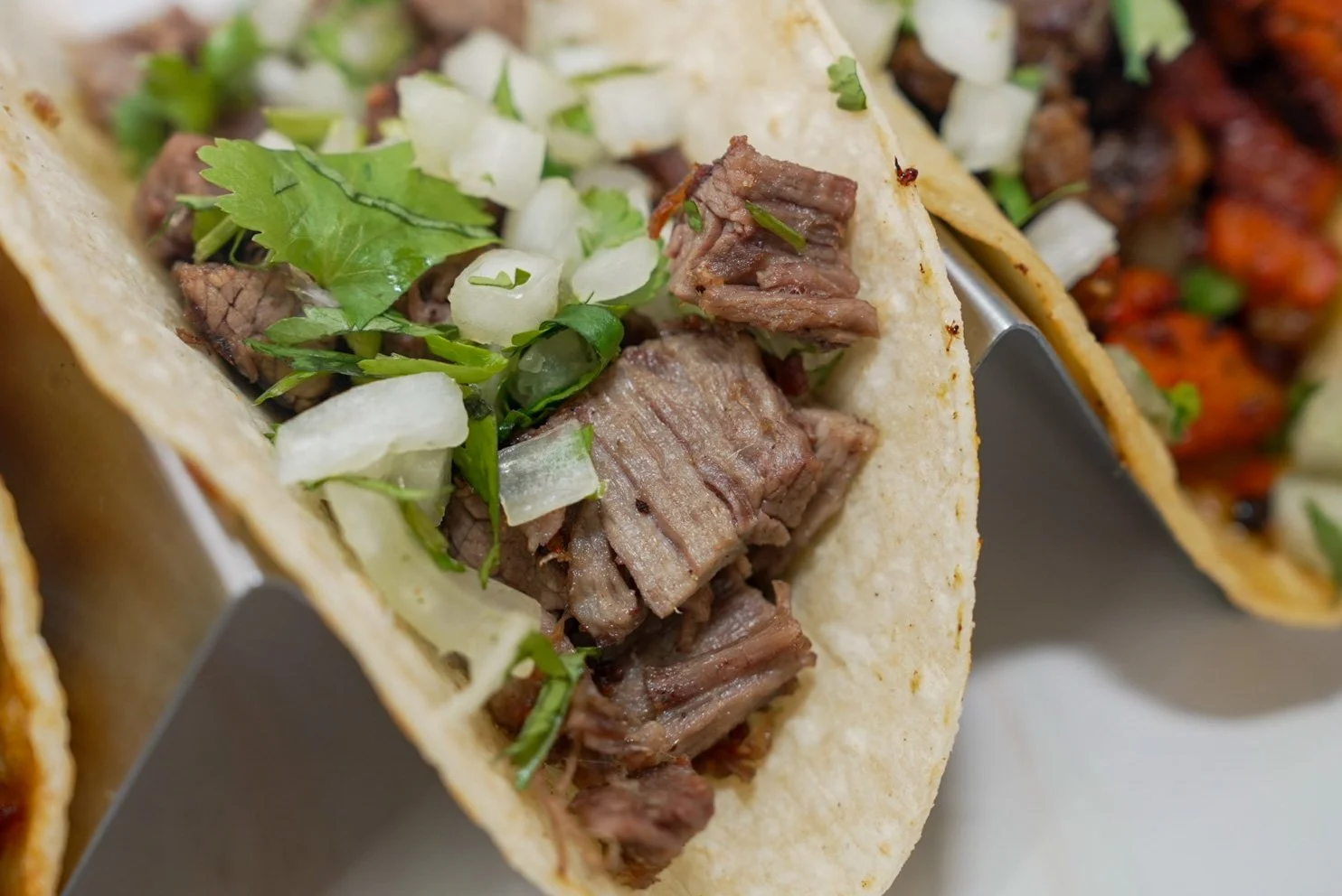 Close-up of a beef taco with chopped onions, cilantro, and diced cooked beef in a soft corn tortilla.