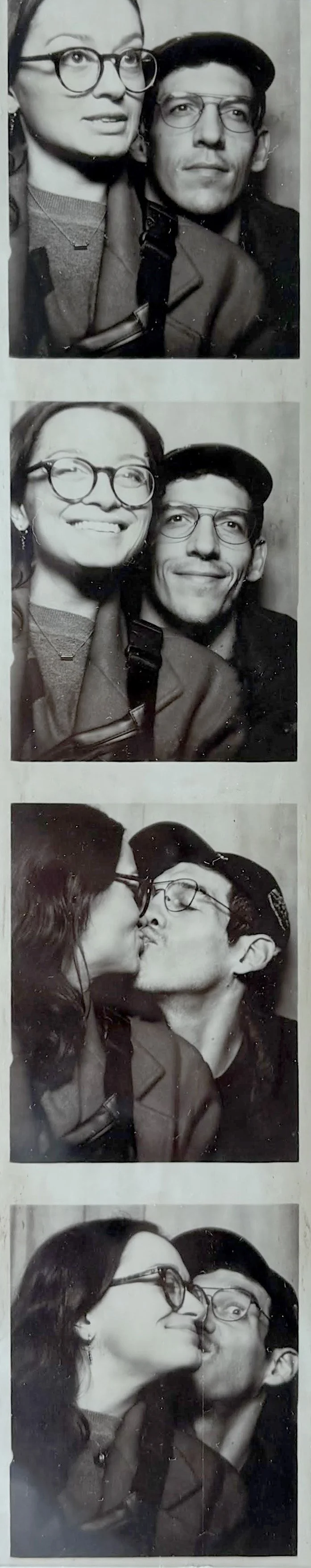 A series of black-and-white photo booth strips showing a man and woman with glasses. In the first photo, they pose side by side with neutral expressions. In the second, they smile widely. In the third, they kiss, and in the last, they are close with playful expressions.