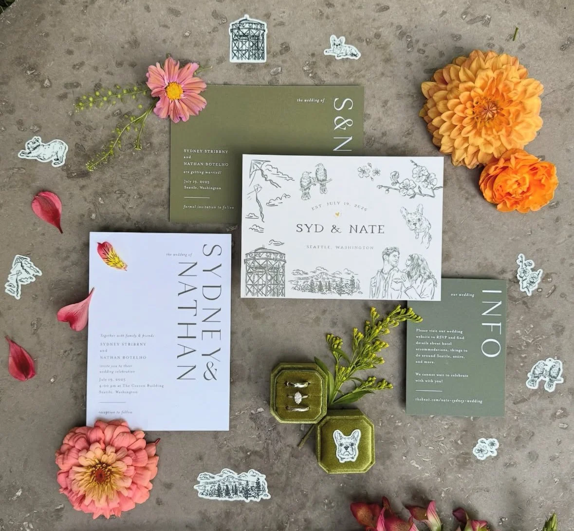 Wedding invitations with floral and animal-themed stickers, flowers, and a small ring box on a concrete surface.