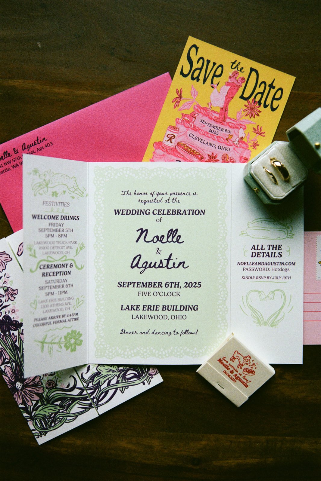 Wedding invitation, save the date card, and accessories for a wedding celebration, including rings in a box and a small favor box, arranged on a wooden surface.