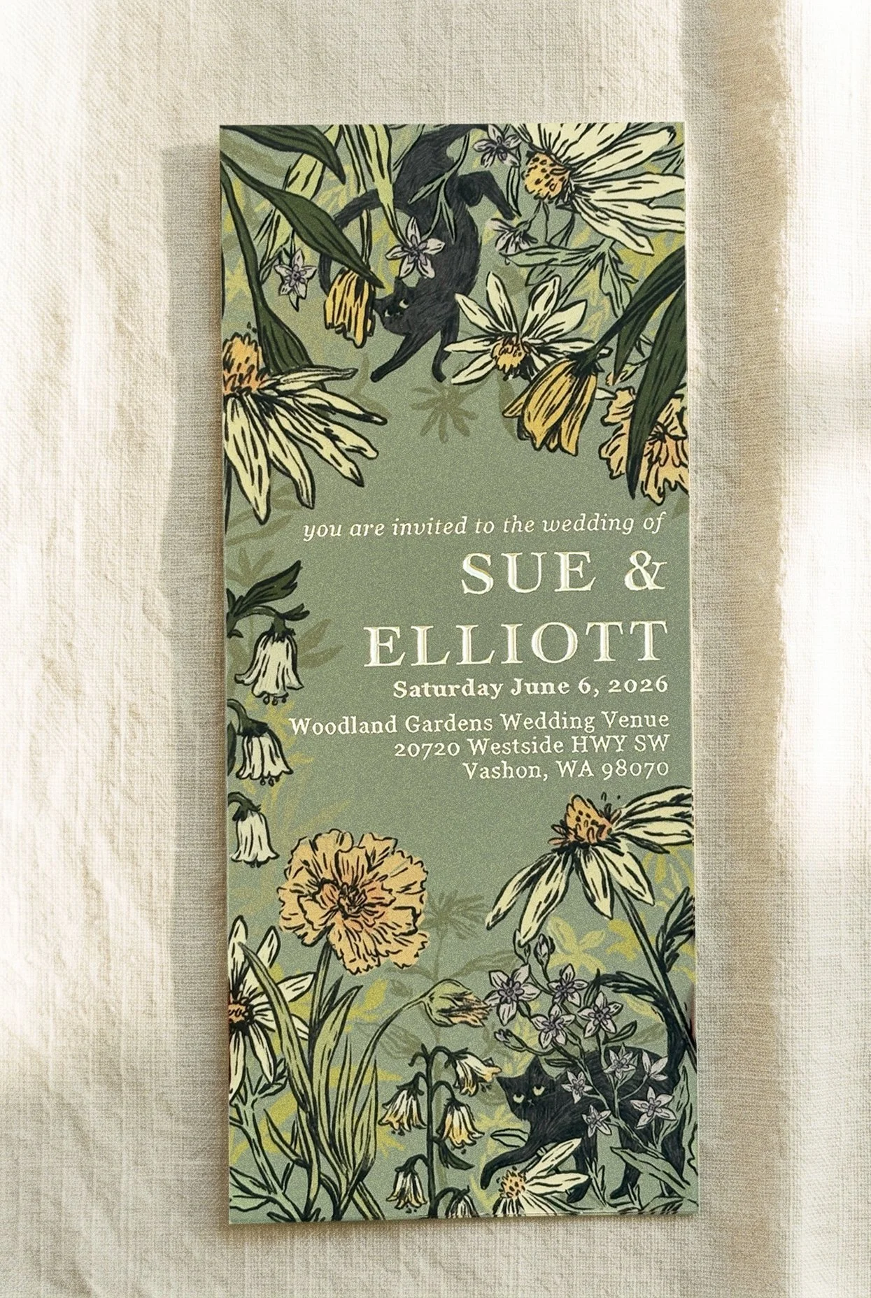 Wedding invitation card with floral illustrations and a black cat, announcing the wedding of Sue and Elliott on June 6, 2026, at Woodland Gardens Wedding Venue in Vashon, Washington.