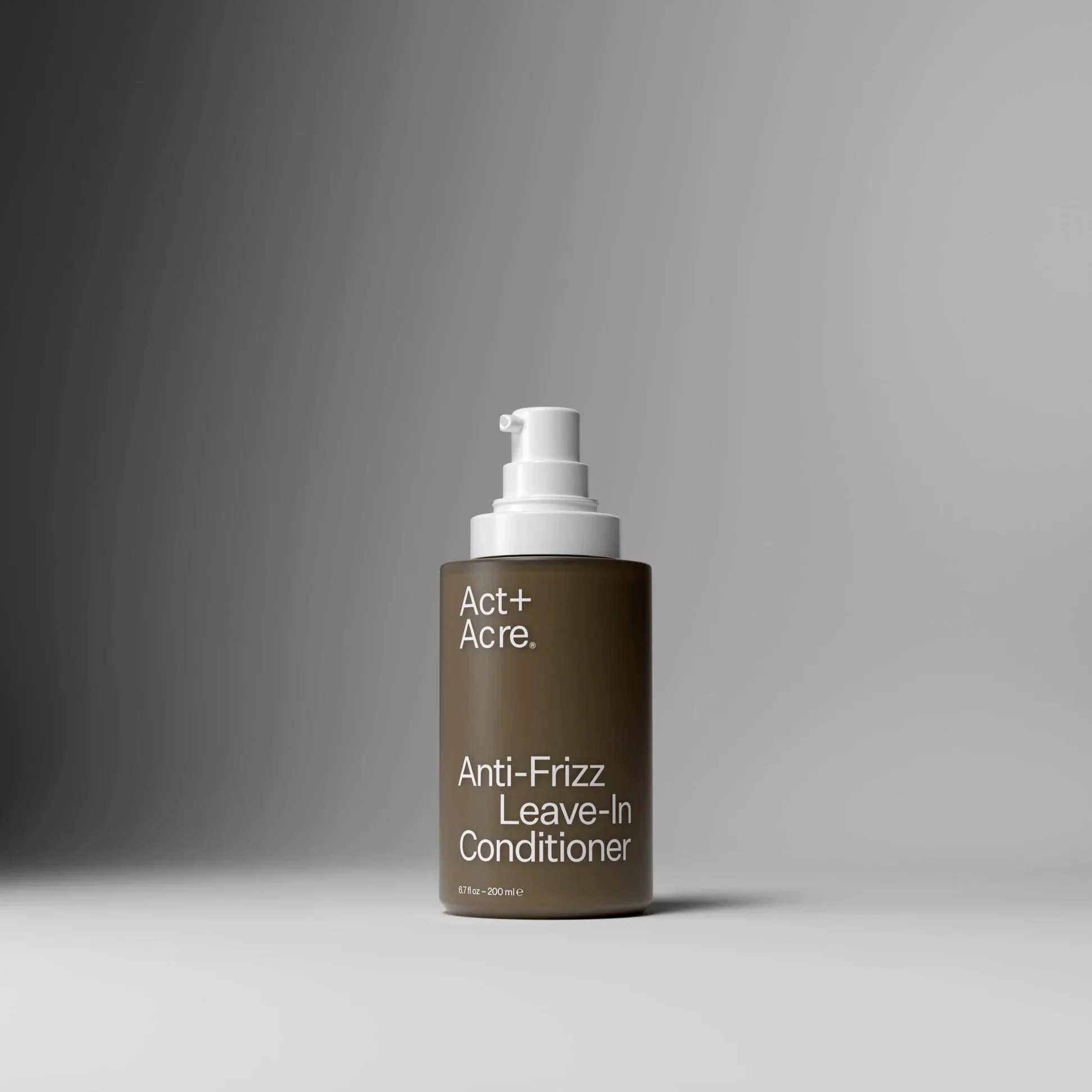 A bottle of Act+ Acre Anti-Frizz Leave-In Conditioner on a gray background.