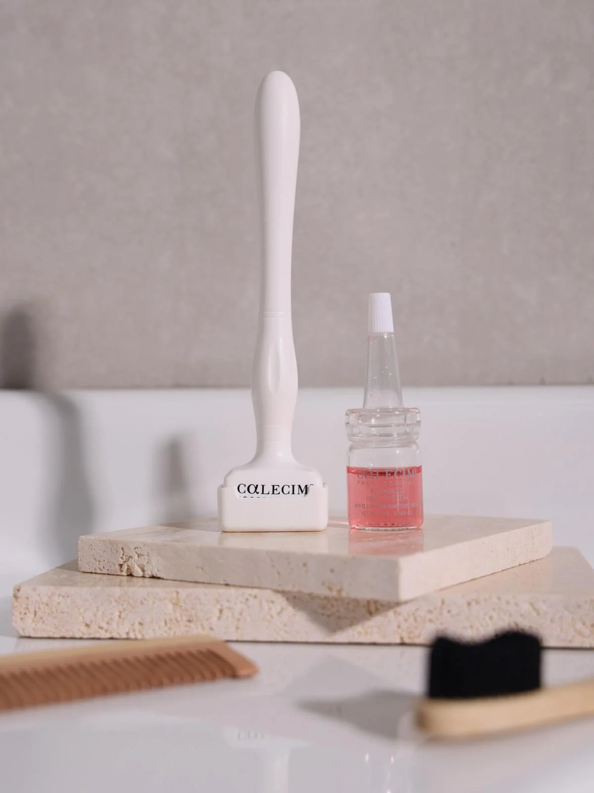 A white toothbrush with black text on its base, and a small glass bottle with pink liquid, sitting on a beige stone surface.