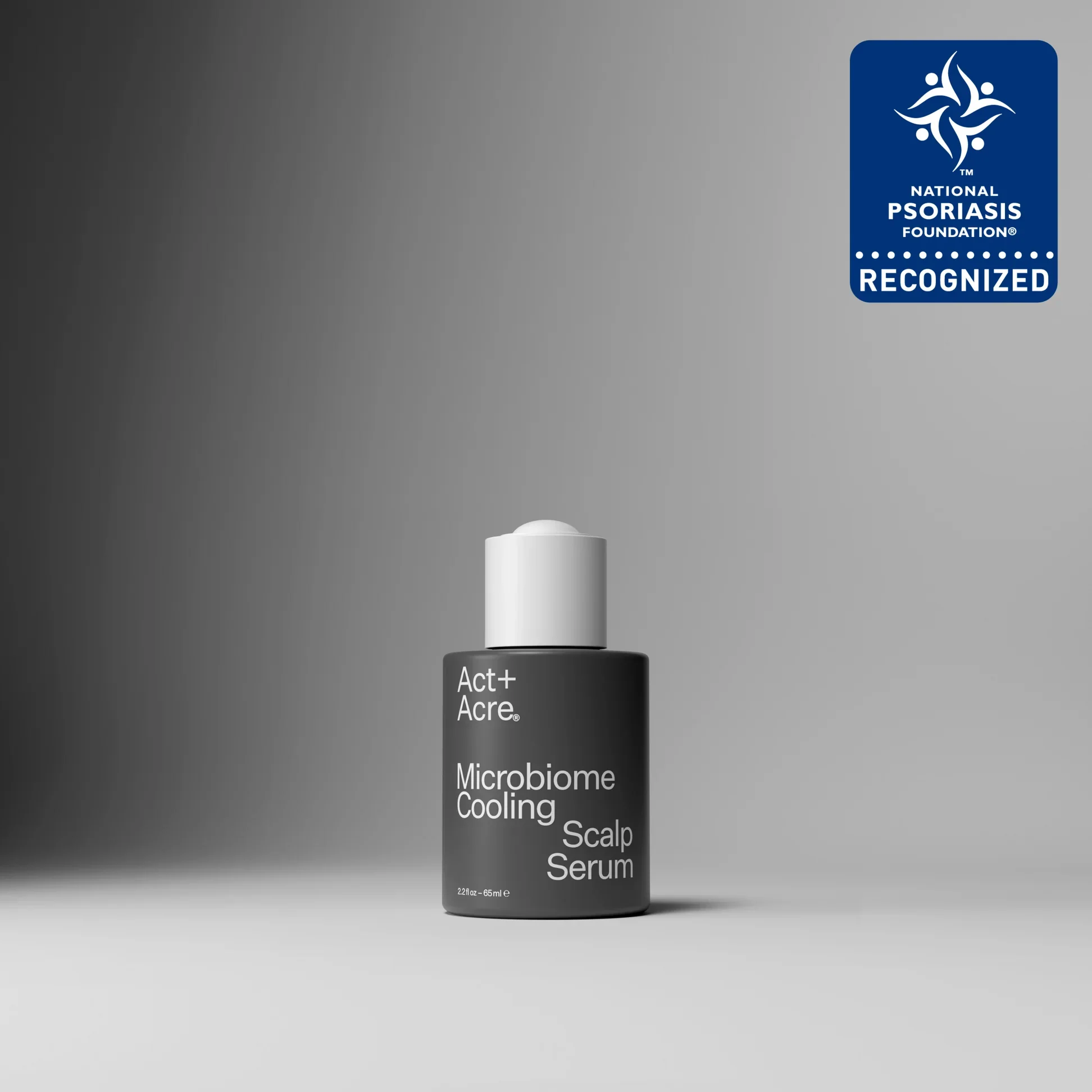 A skincare serum bottle labeled 'Act+ Acre Microbiome Cooling Scalp Serum' on a gray background, with a blue certification sticker indicating recognition from the National Psoriasis Foundation.