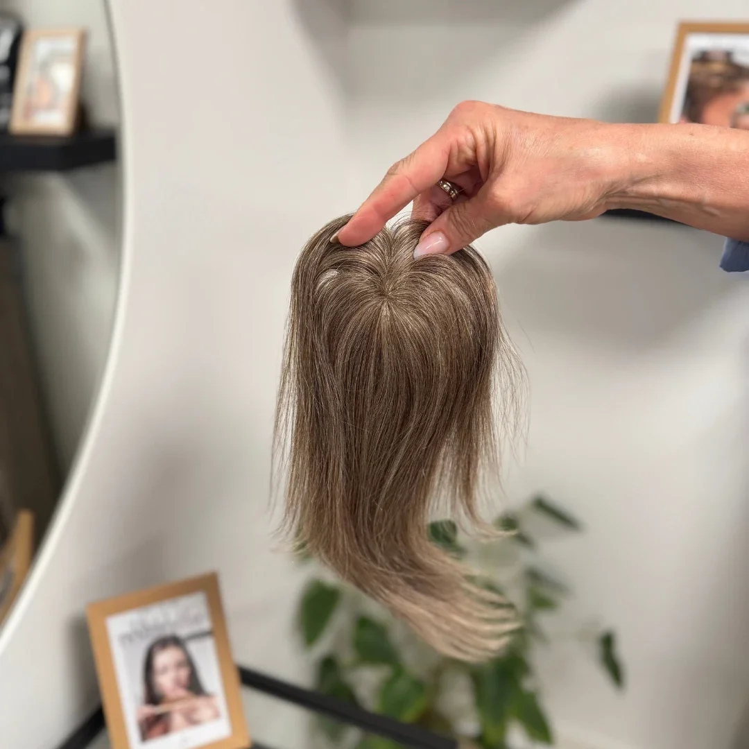 A hand holding a mannequin hairpiece with brown hair.