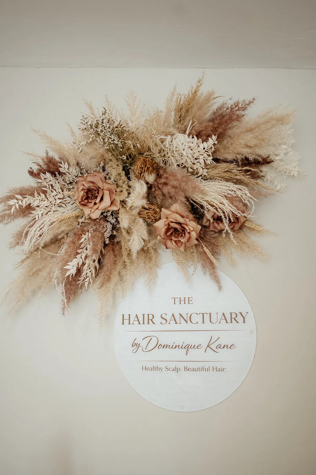 Dried flower arrangement with roses and pampas grass above a sign that reads 'The Hair Sanctuary by Dominique Kane, Healthy Scalp. Beautiful Hair'.