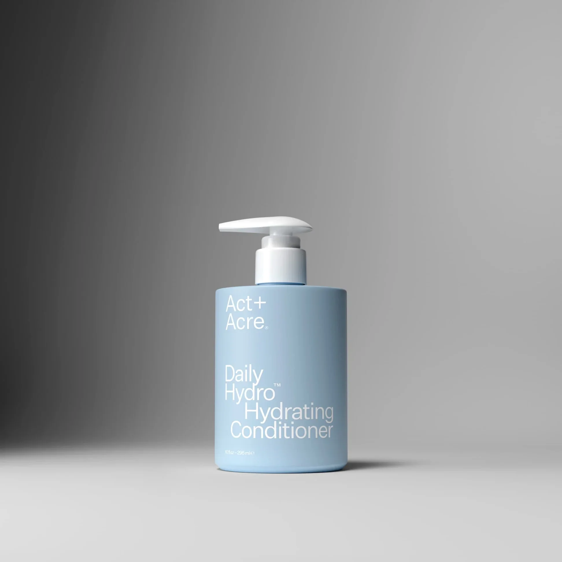 A bottle of Act+ Acre Daily Hydrating Conditioner against a gray background.
