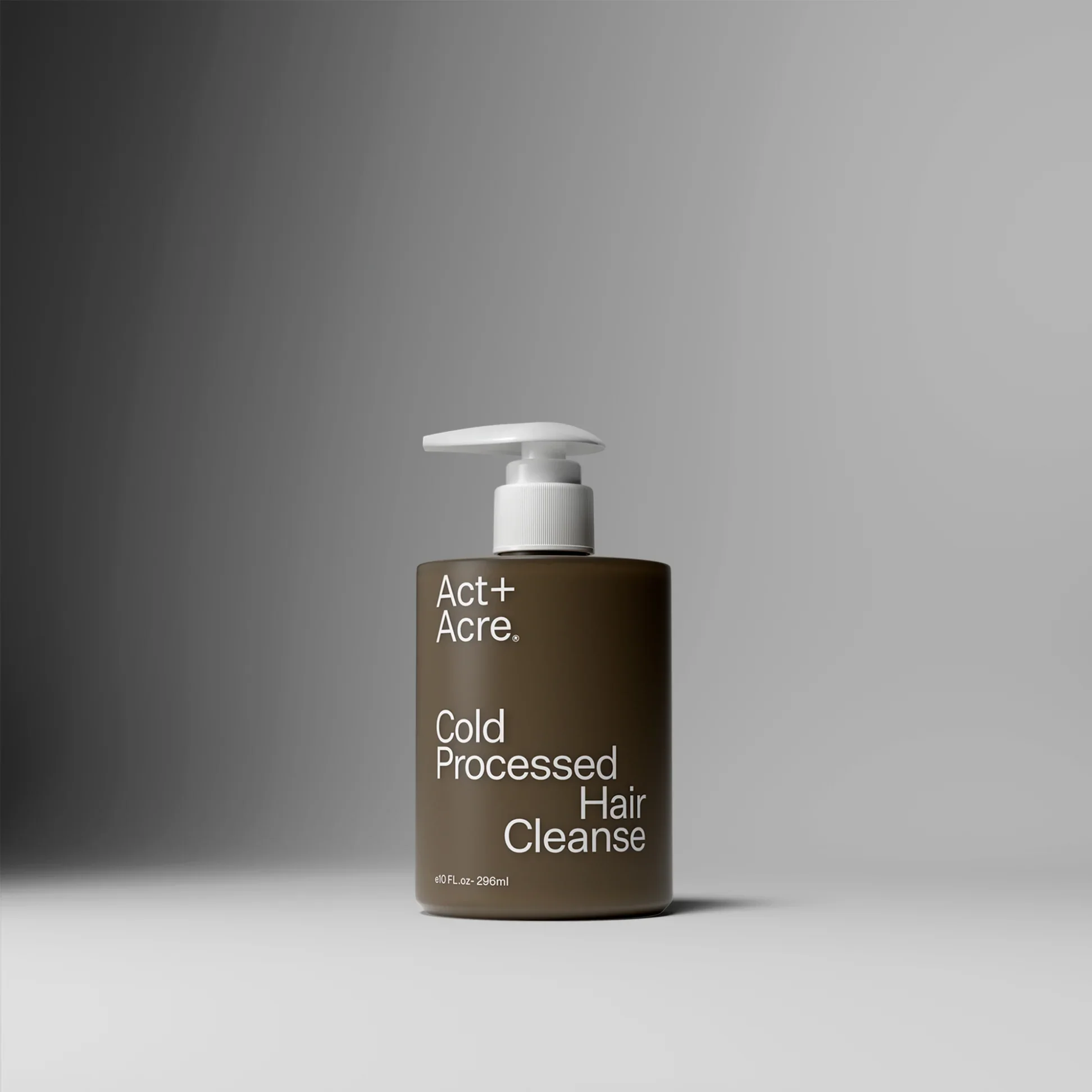 A black bottle with a white pump dispenser labeled 'Act+ Acre' that contains a hair care product. The bottle has white text listing the product as a 'Cold Processed Hair Cleanse' with a volume of 10 fluid ounces or 296 milliliters. The background is a plain, gradient gray.