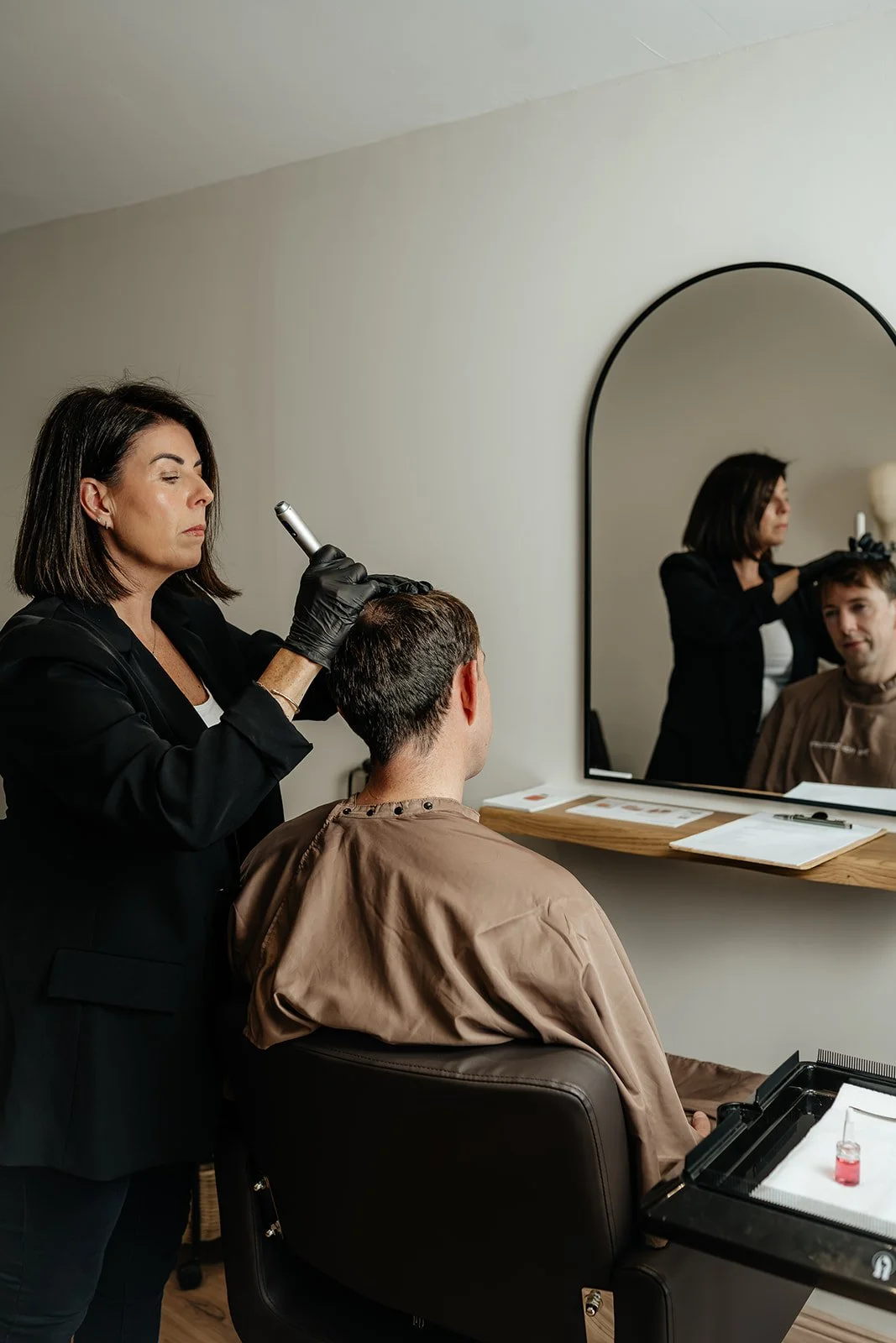 A woman with blond hair lying back in a salon wash basin while a stylist rinses her hair with a handheld showerhead.