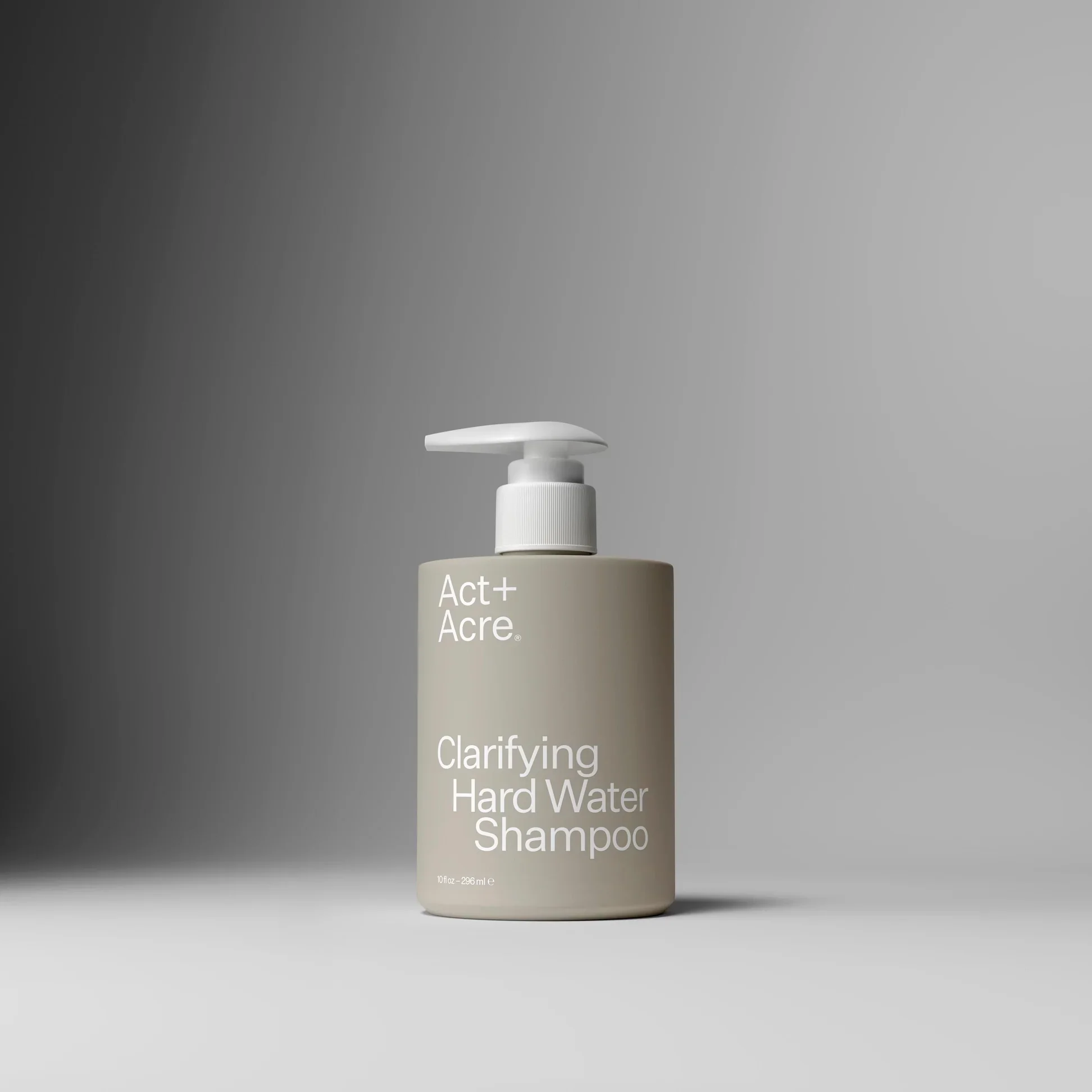 A gray bottle of Act+ Acre Clarifying Hard Water Shampoo with a pump dispenser, set against a gray background.