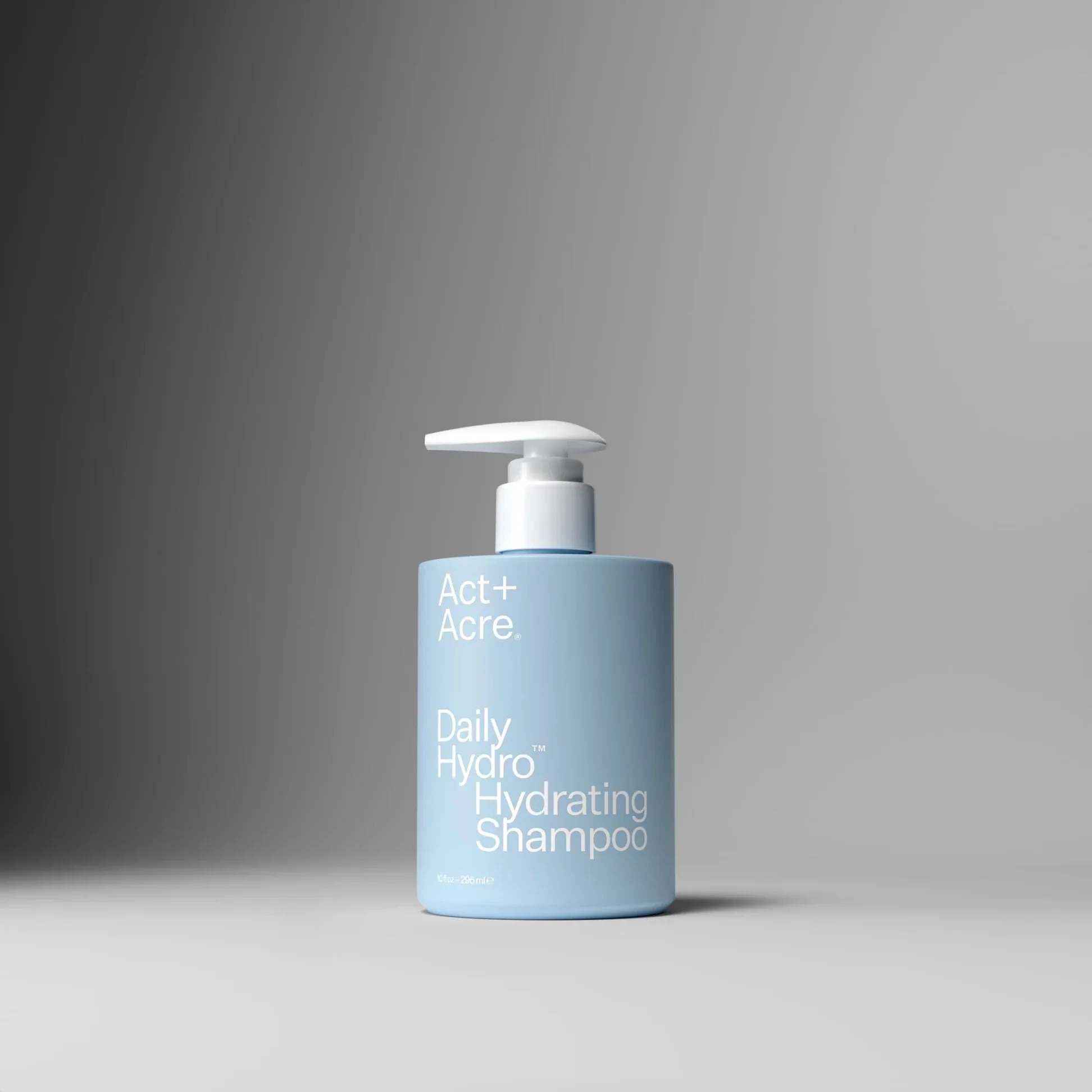 Light blue bottle of Act+ Acre Daily Hydrating Shampoo with white pump dispenser against a gray gradient background.