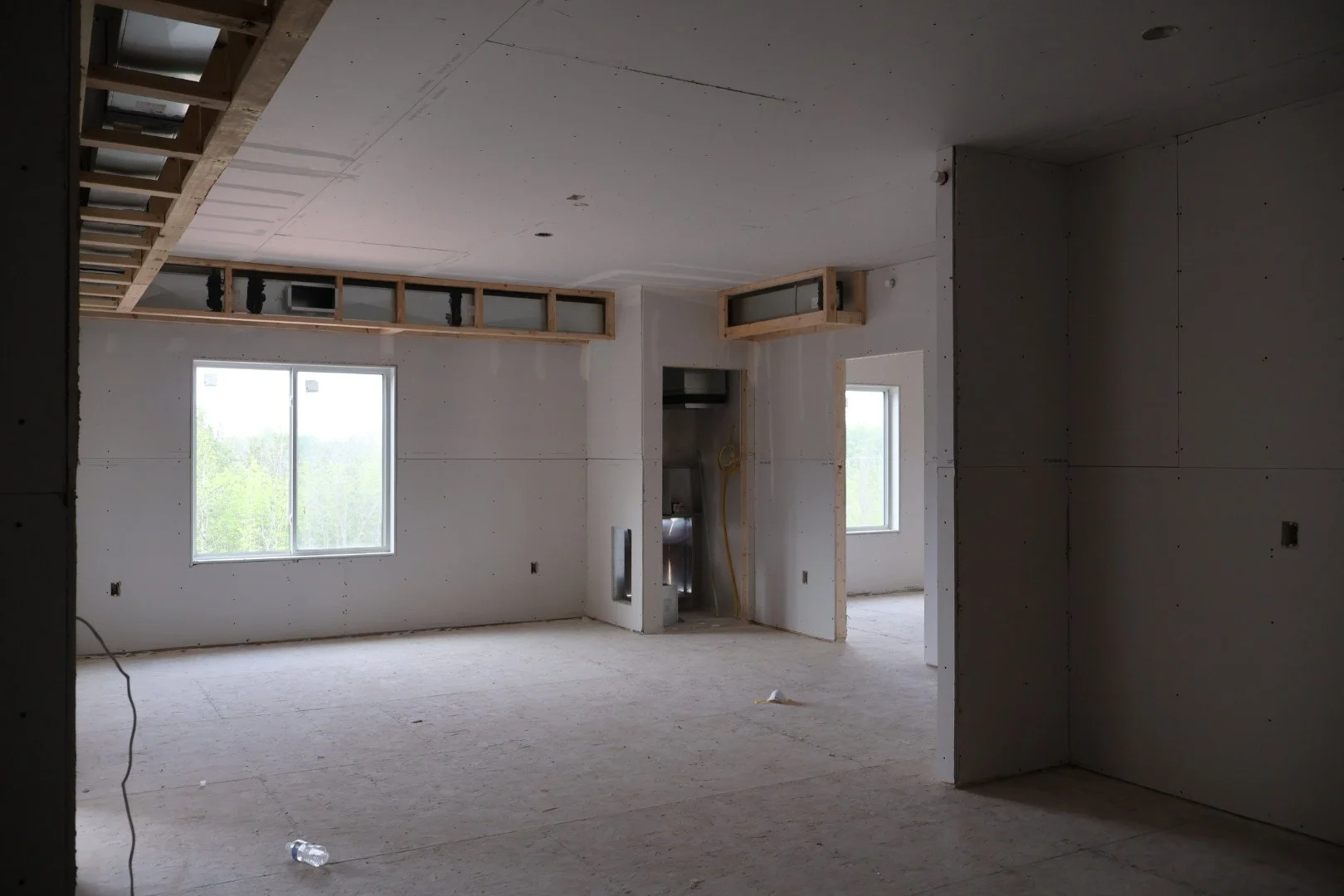 Interior of a room under construction with unfinished drywall walls, open window, and visible framing for ceiling and walls.