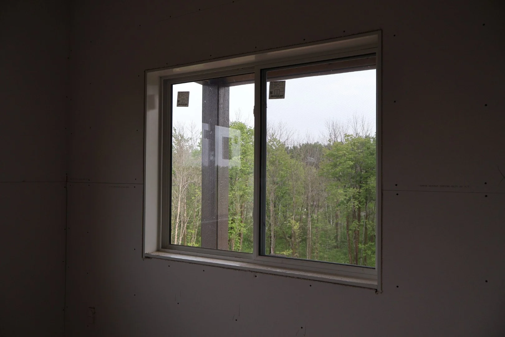 Unfinished interior wall with a window showing a view of trees and a cloudy sky outside.