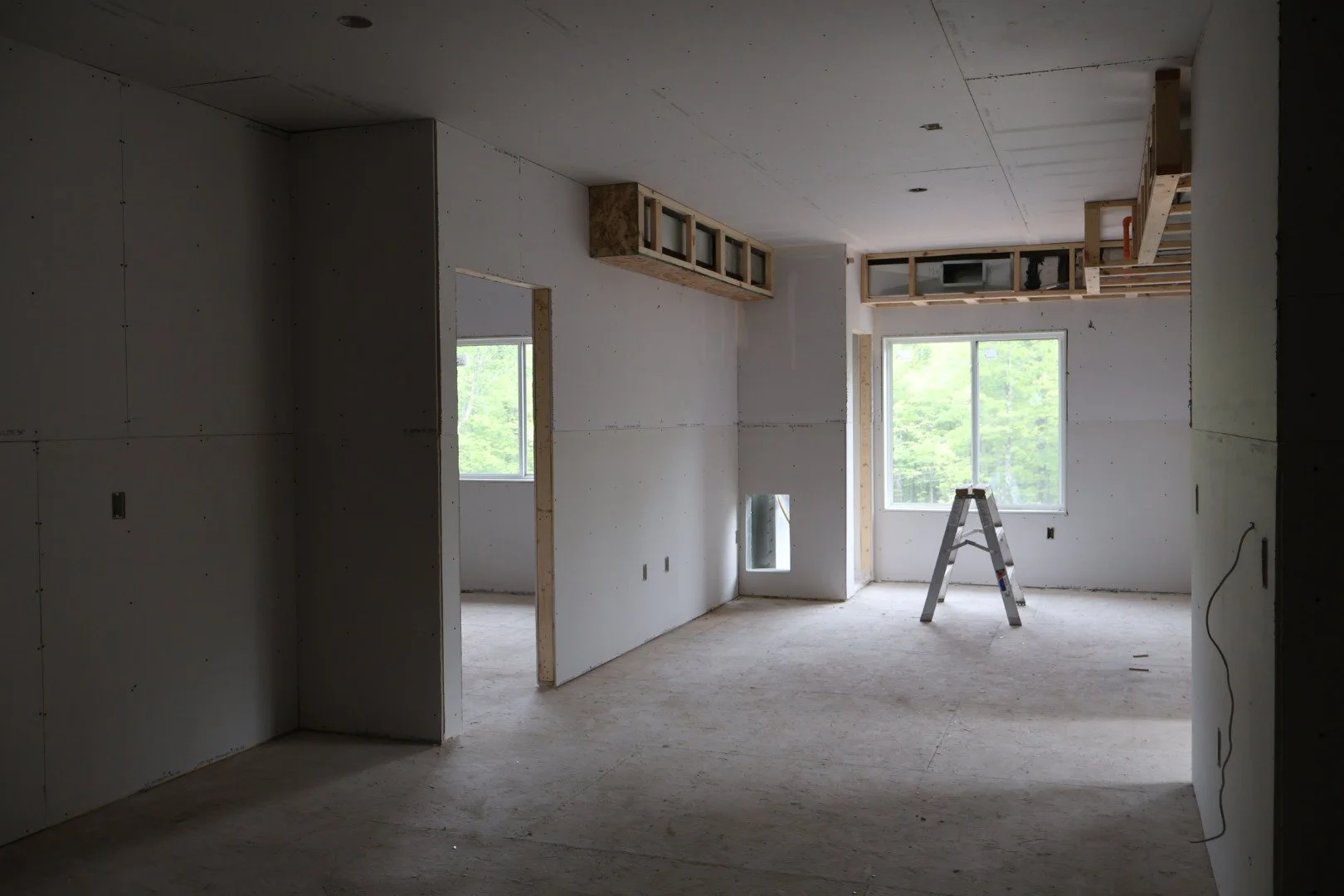Interior of an unfinished house under construction with drywall walls, windows, and a ladder.