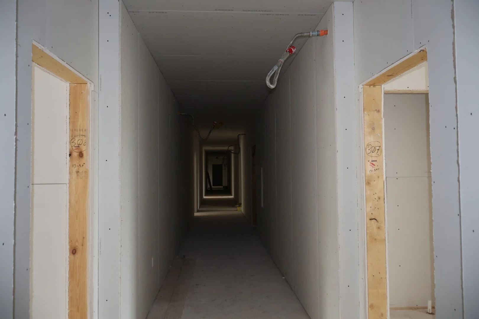 Long narrow hallway under construction with framed doorways and electrical wiring visible on the ceiling.