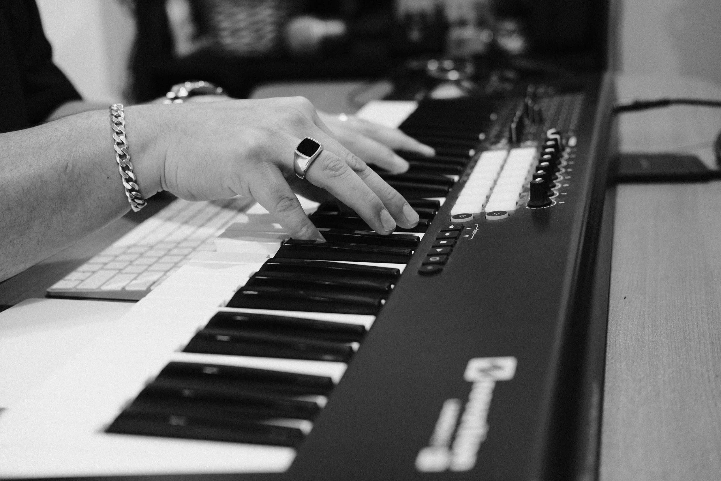Close-up of a person's hand wearing a bracelet and ring, playing a keyboard or synthesizer, with various controls and keys visible.