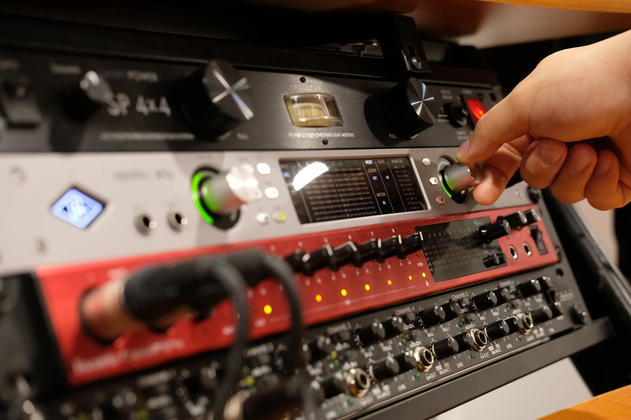 Close-up of a DJ's hand adjusting a knob on a mixing console with multiple knobs, buttons, and meters visible.