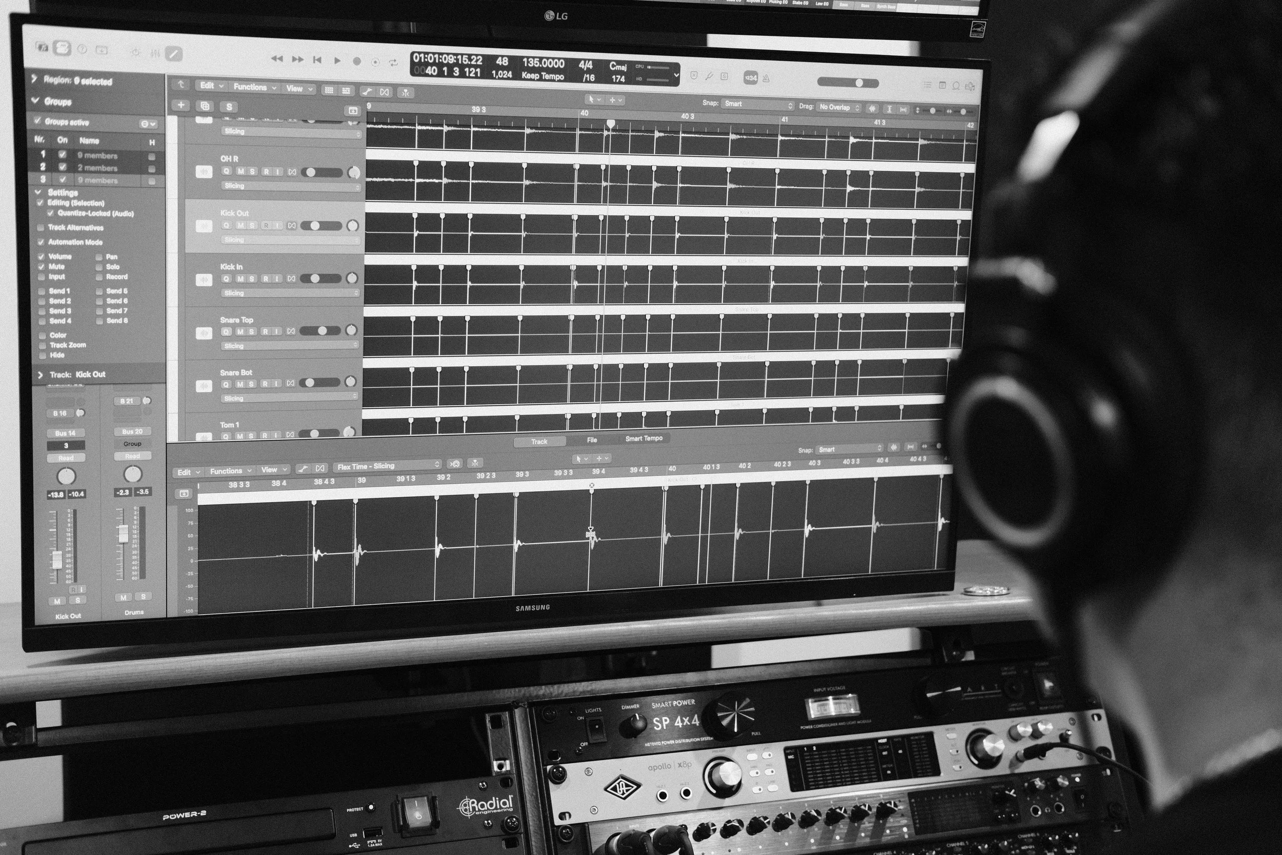 Black and white photograph of a computer monitor displaying music production software with multiple audio tracks and waveforms. Below the monitor, audio equipment and controls are visible.