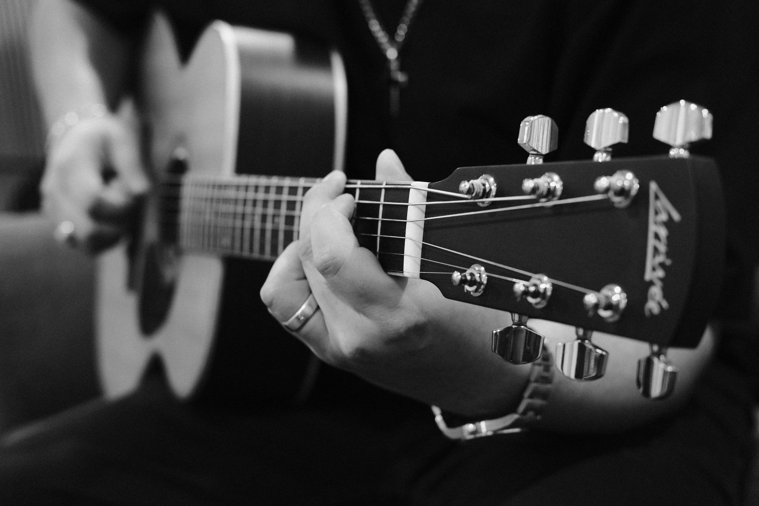 Close-up of a person playing an acoustic guitar, focusing on their hand on the fretboard and the tuning pegs.