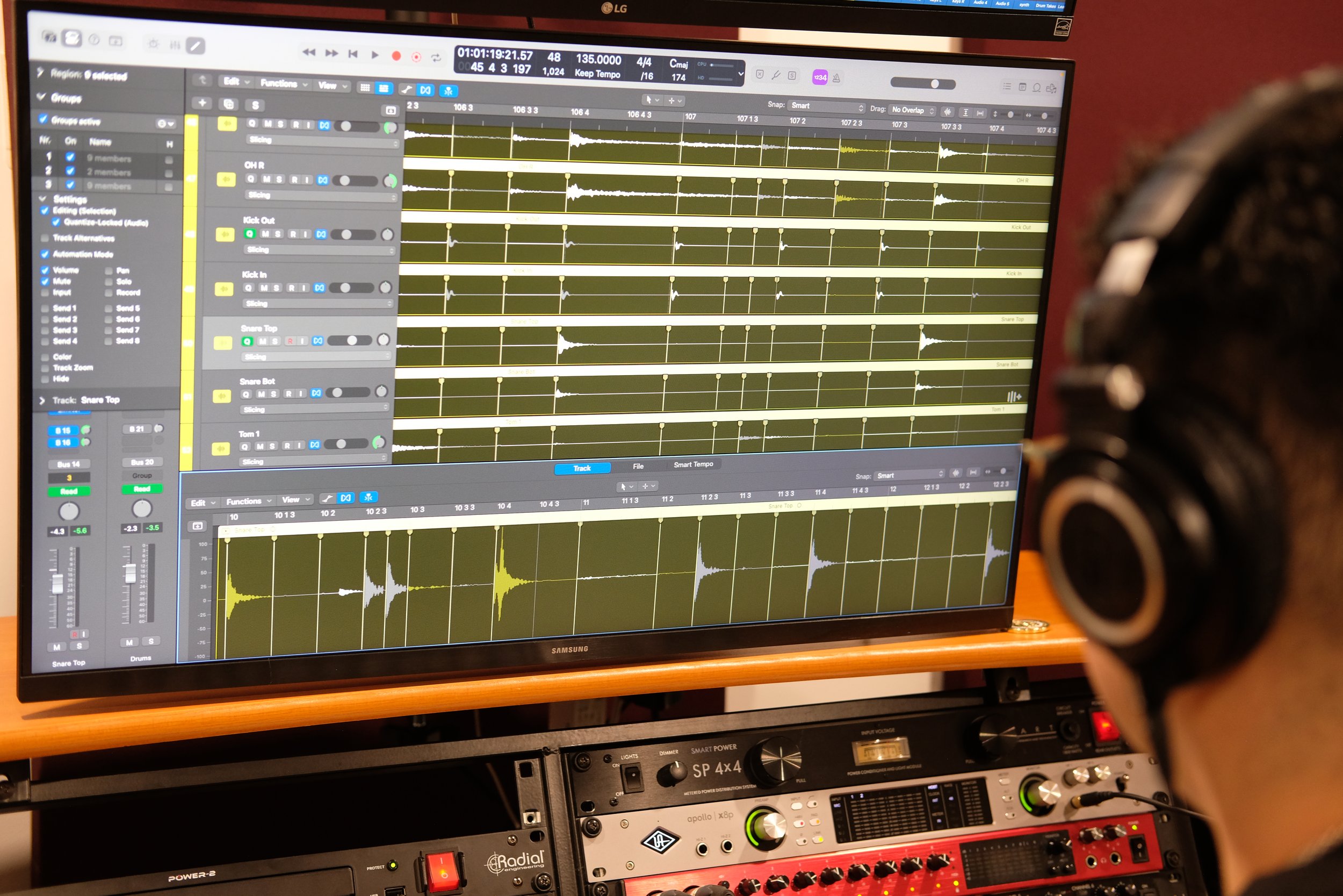 A computer monitor displaying sound editing software with multiple audio waveforms and tracks. Below the monitor are audio equipment and mixers.