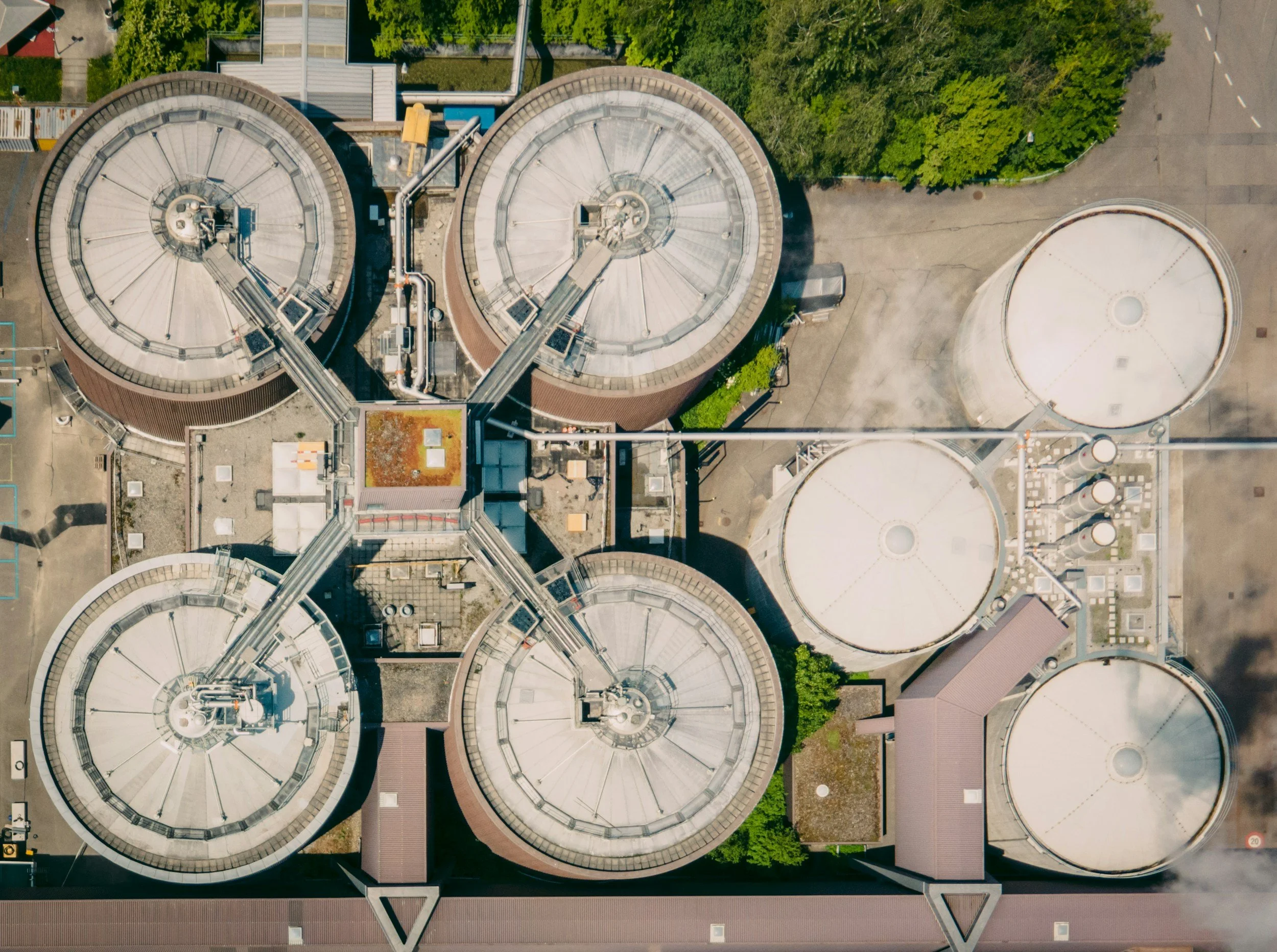 Aerial view of an industrial facility with multiple large, circular cooling towers and interconnected pipes and structures.