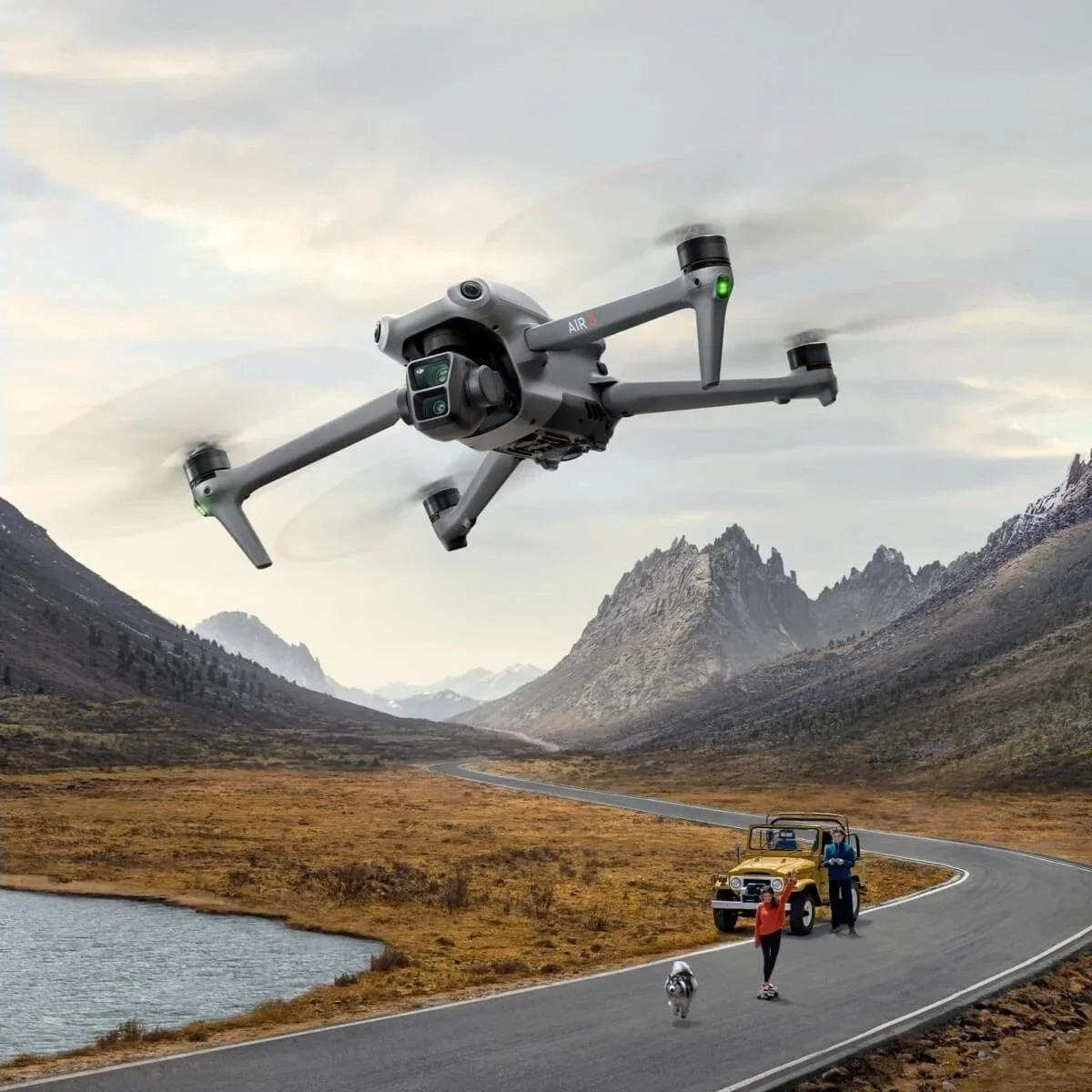 A drone flying over a mountain valley with a car, a woman roller skating, a man, and a dog on the road.