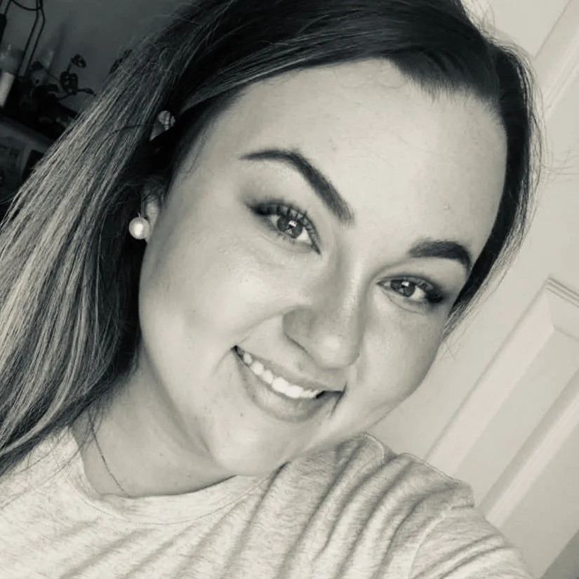 A young woman with long hair, wearing pearl earrings and a light-colored shirt, smiling in a selfie.