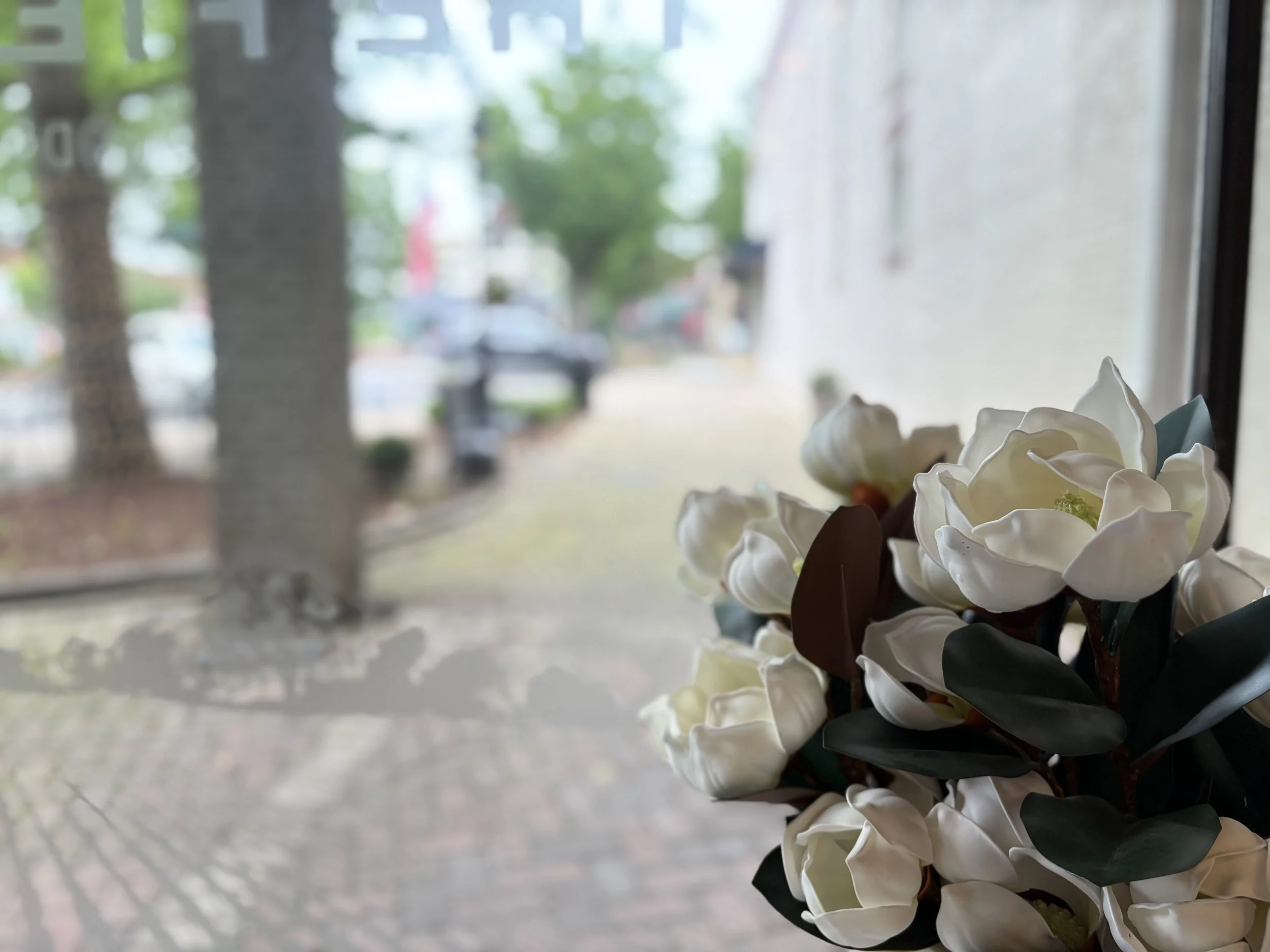 A bouquet of white flowers, possibly artificial, resting on a windowsill. The background shows blurred trees and parked cars outside.