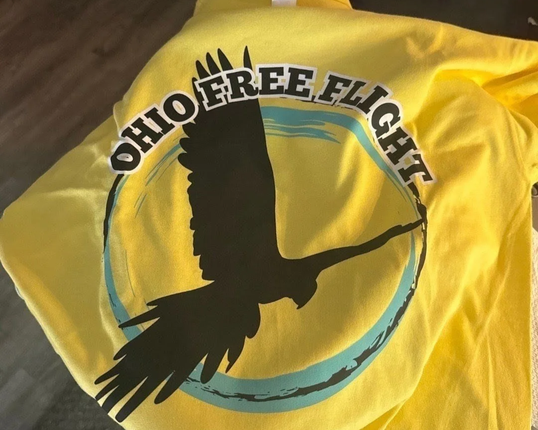 Yellow T-shirt with the Ohio Free Flight logo featuring a silhouetted bird in mid-flight inside a blue and yellow circle.