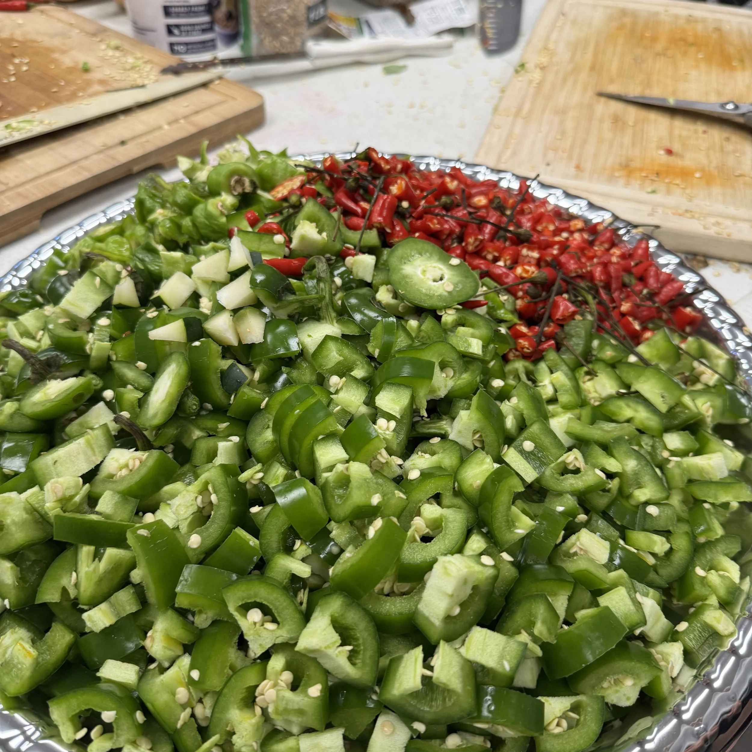 Chopped green peppers and red chili peppers on a decorative plate in a kitchen setting with cutting boards and kitchen utensils in the background.